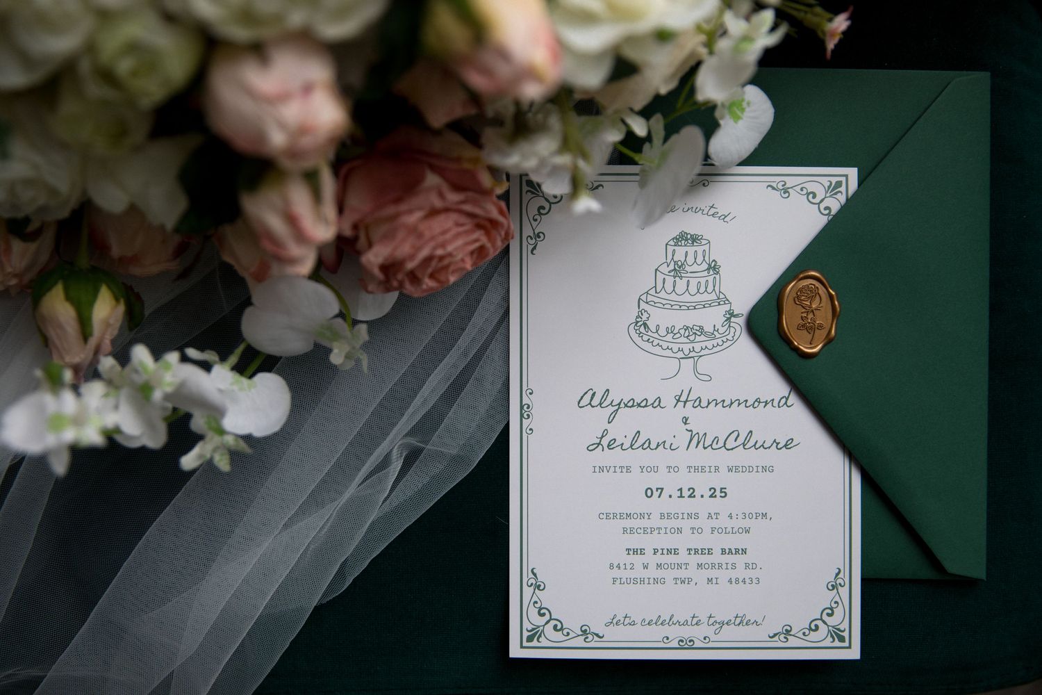 Wedding invitation suite with elegant floral design and emerald green accents displayed with pink roses and decor.