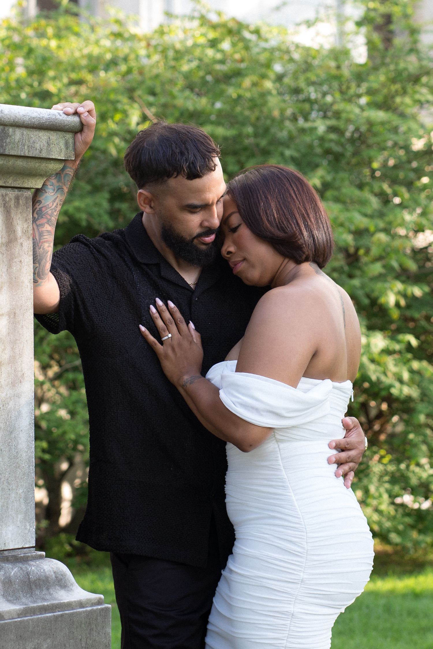 A romantic couple embraces outdoors, with one person wearing black and the other in a white dress.