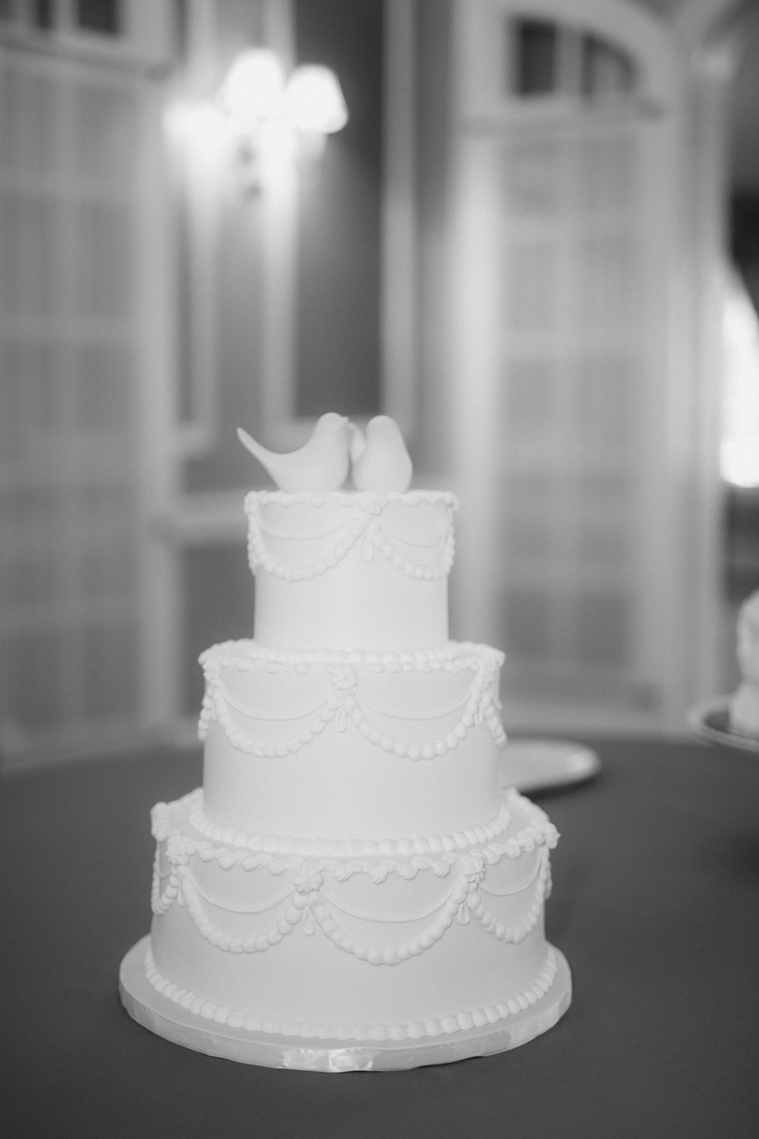 A sequence of five black and white photos showing a classic white wedding cake with delicate piped details and pearl borders.