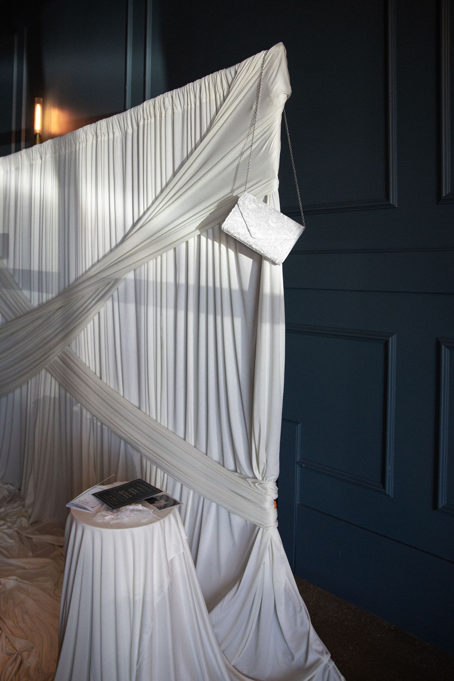 White draped fabric backdrop with elegant lace clutch purse hanging at a wedding venue.