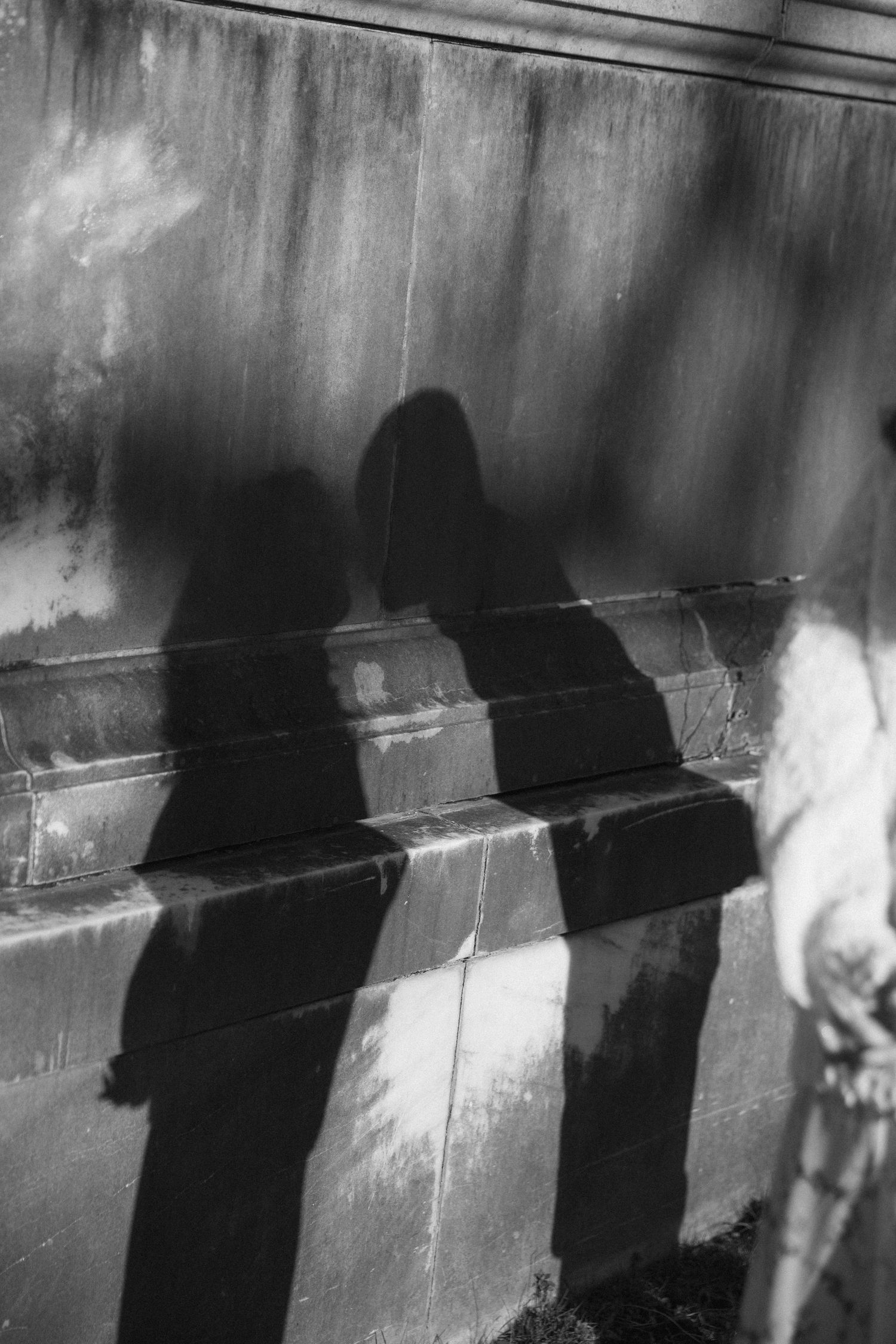 Black and white photo of two people's shadows cast on a stone wall and steps in dramatic sunlight.