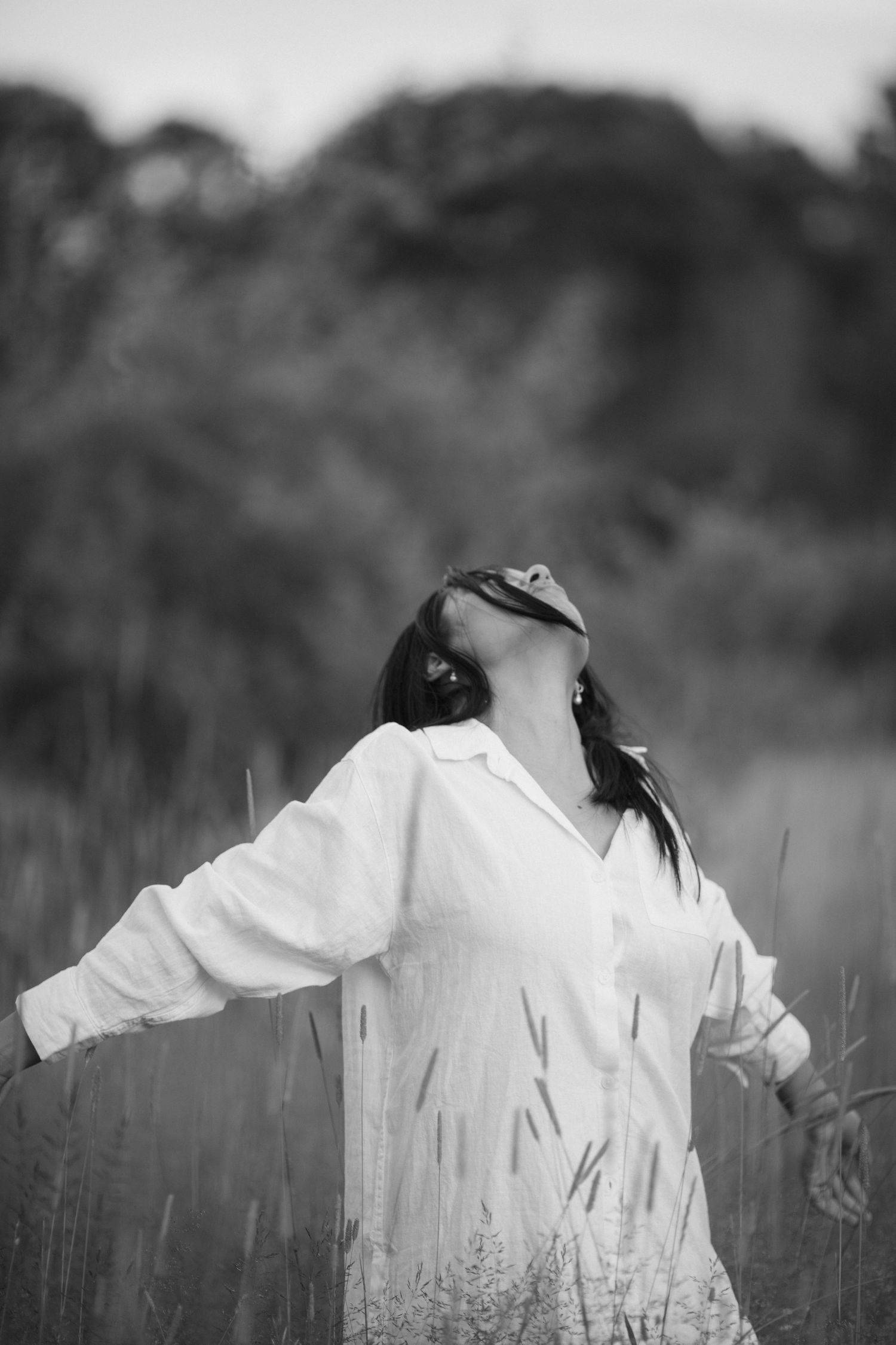 Black and white portrait of a person in a white shirt standing in a field with head tilted back in an expressive pose.