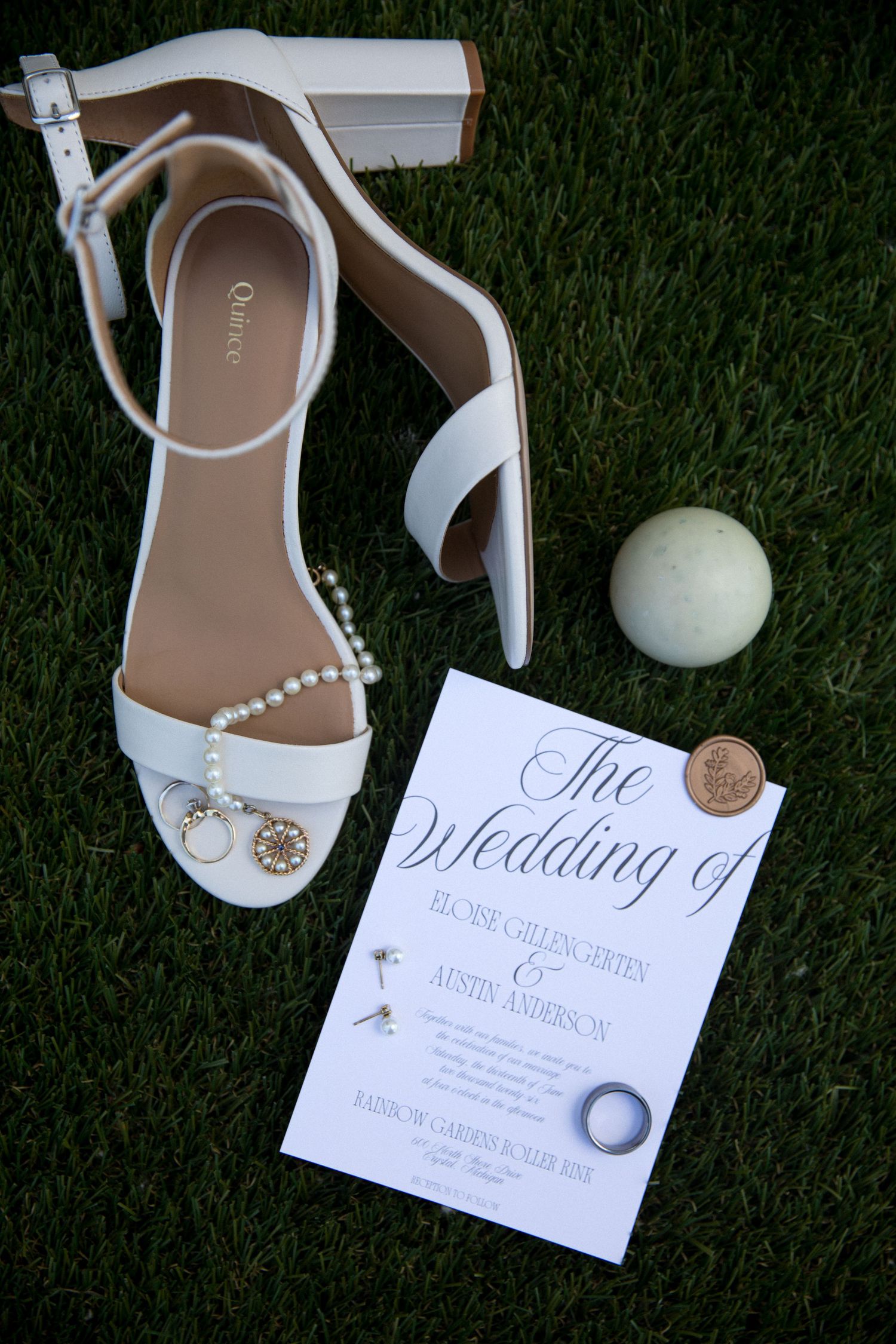 White bridal heels with pearl details and wedding invitation for Eloise and Austin Anderson on green grass.