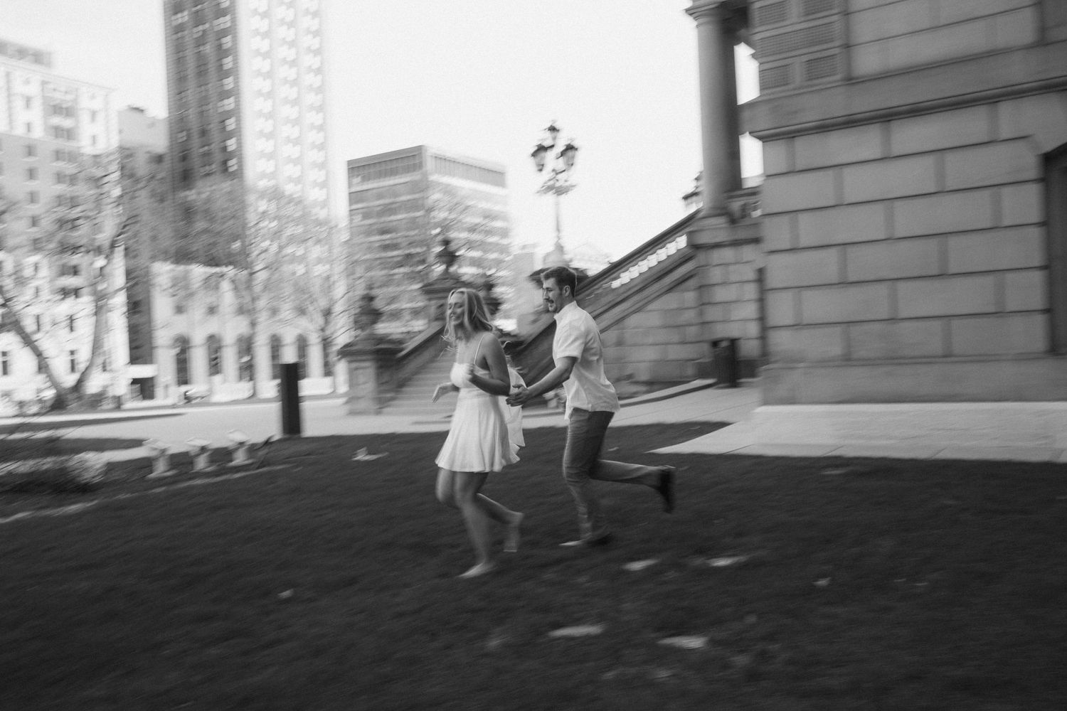 A blurred black and white photo of a couple running playfully near a historic urban building.