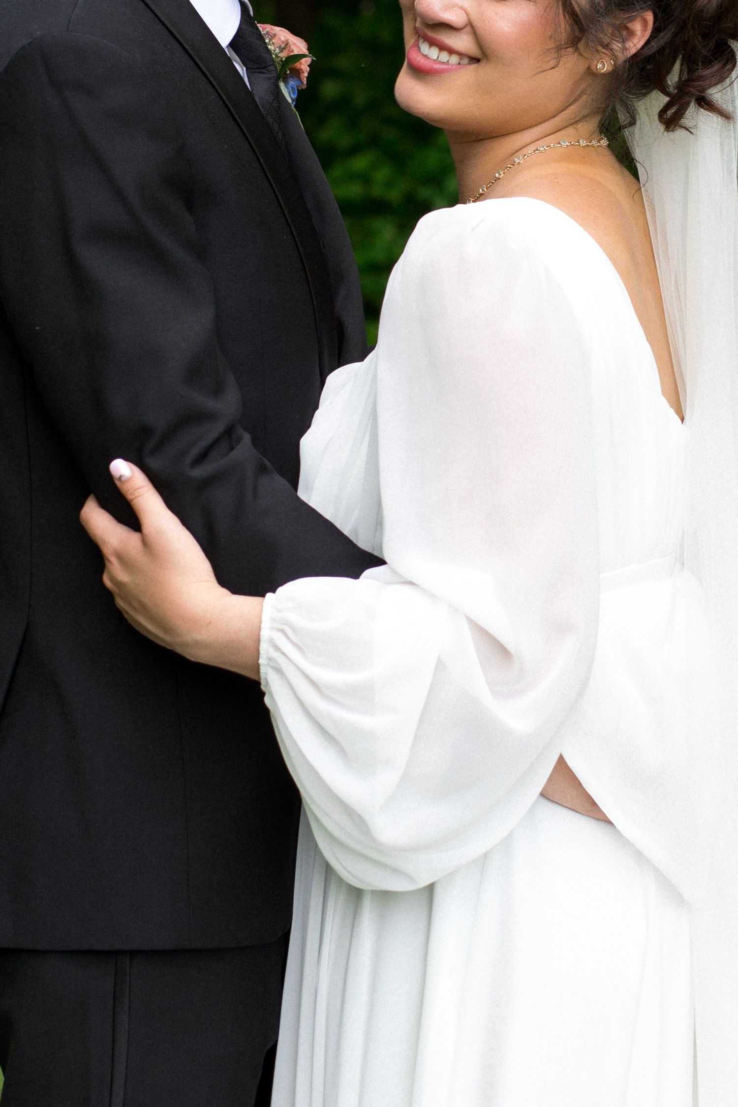 Close-up detail of wedding couple showing white flowing dress sleeve against black tuxedo.