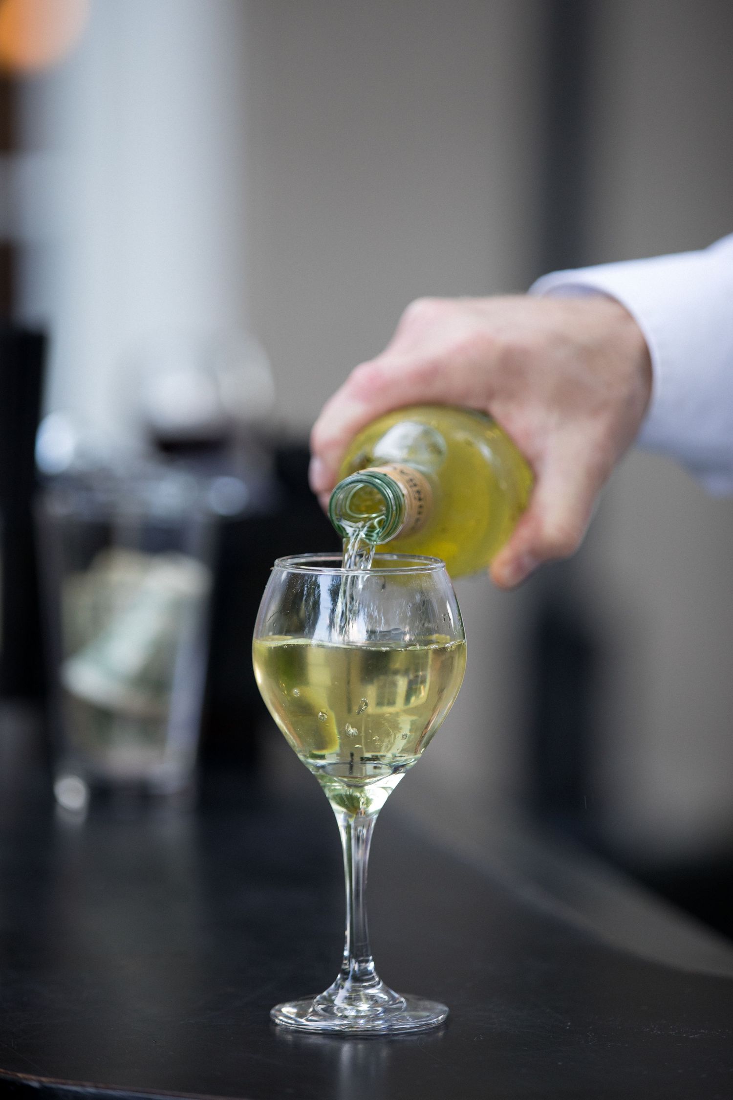 A sequence of images showing white wine being poured into a stemmed glass on a dark surface.