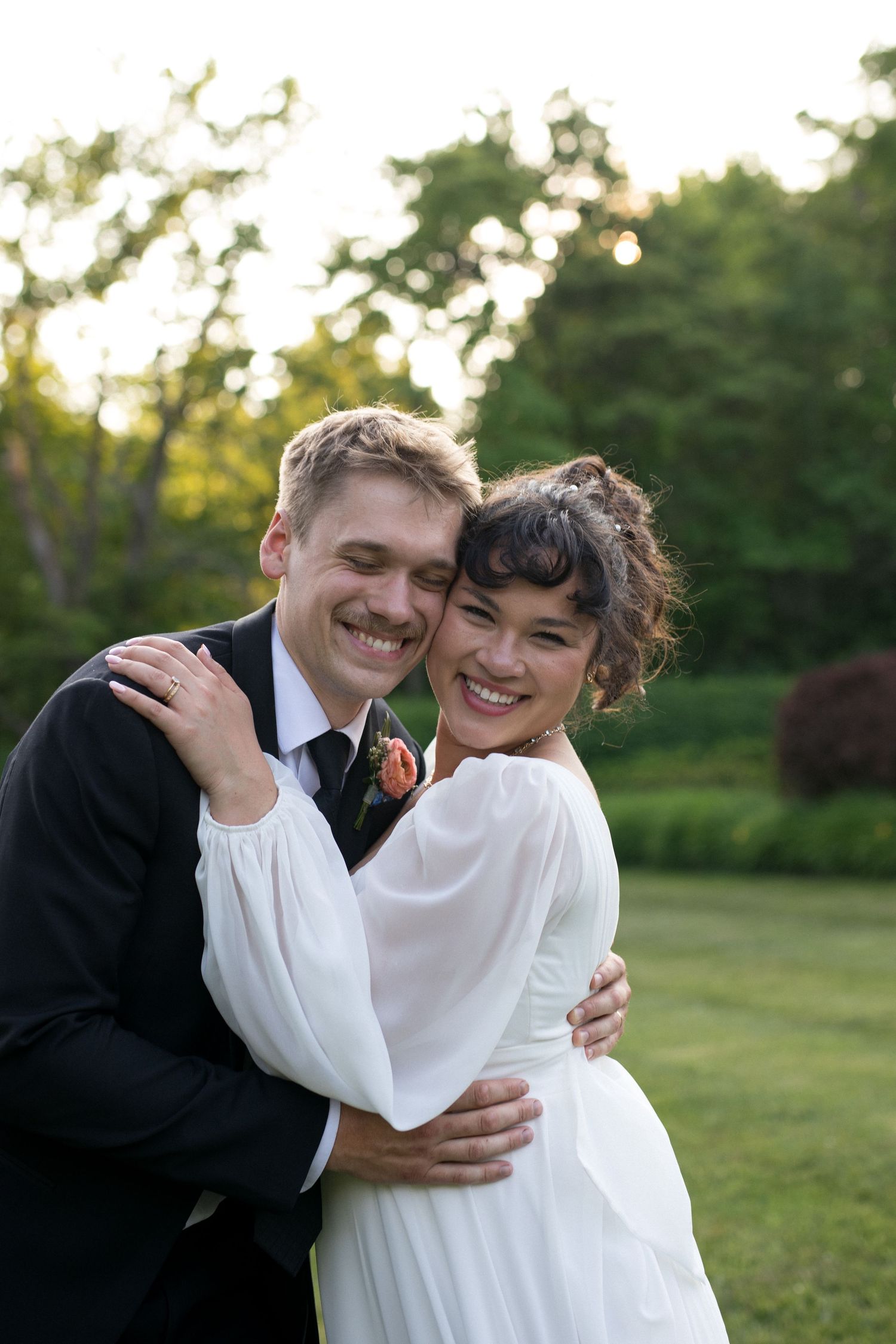 A happy couple embracing in a lush, outdoor setting with trees and greenery in the background.