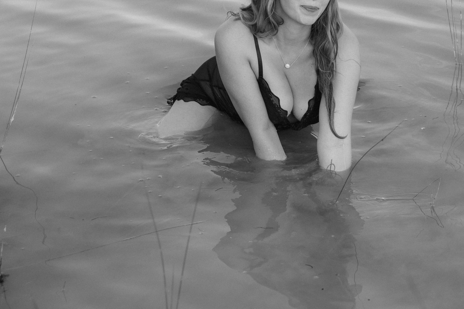 A person in a black swimsuit wades in rippling water, captured in artistic black and white photography.