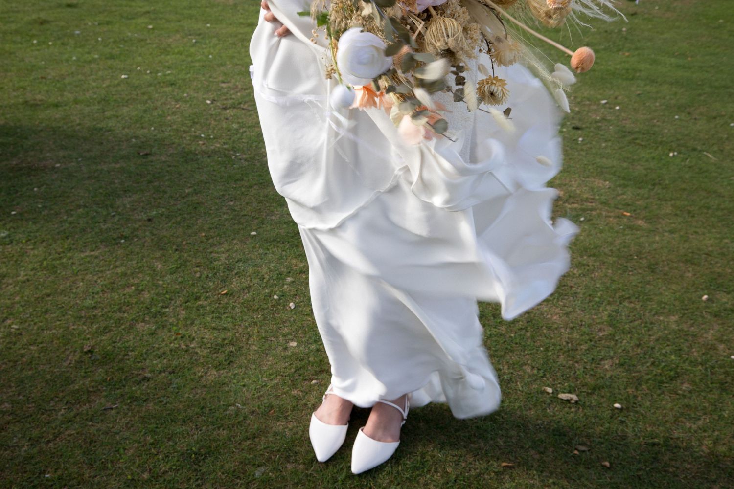 A person in a flowing white dress twirls gracefully on a green lawn, creating a dynamic spinning motion effect.