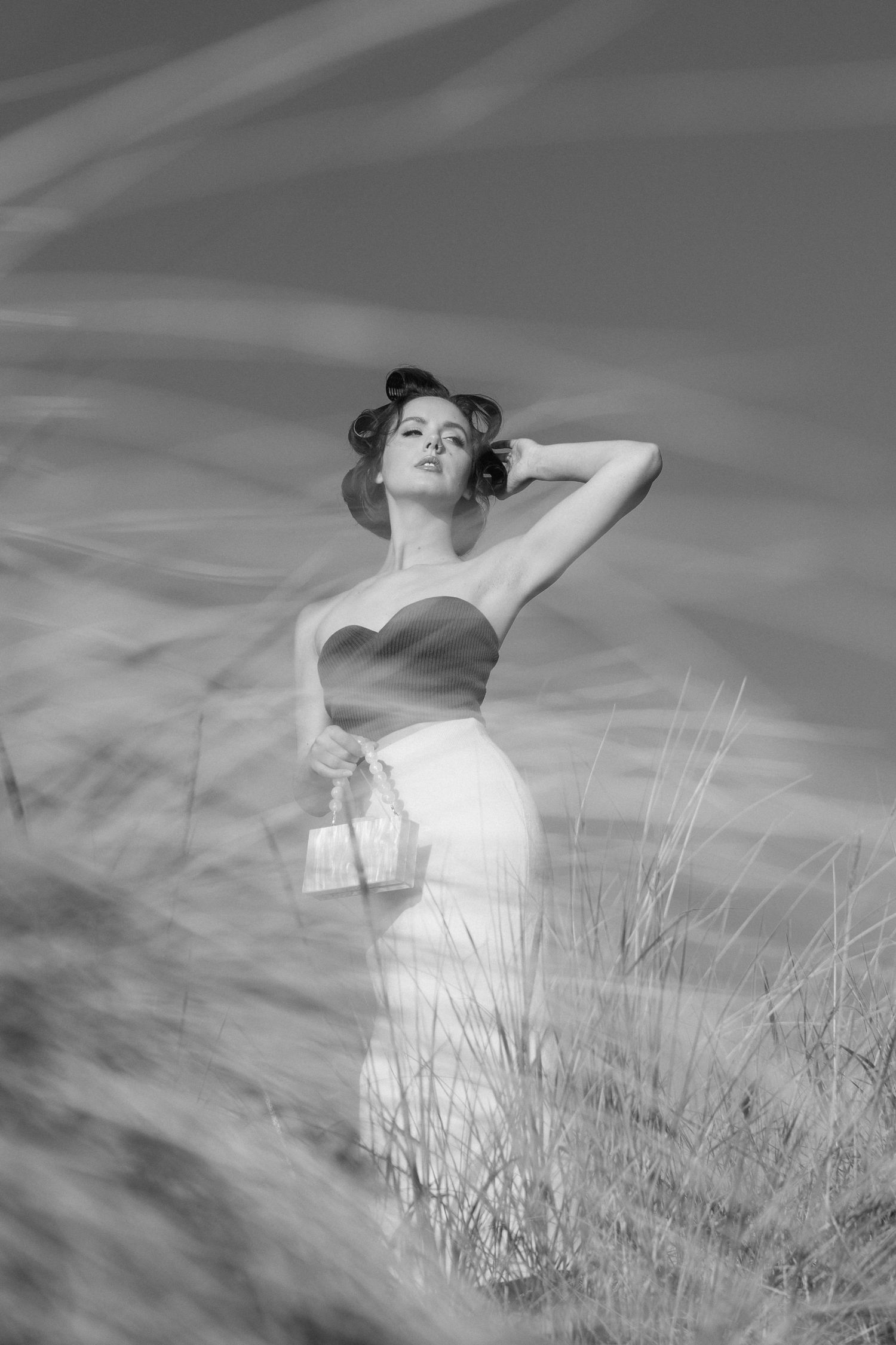 A dreamy black and white sequence shows a figure in white dress reclining in tall grass against a cloudy sky.
