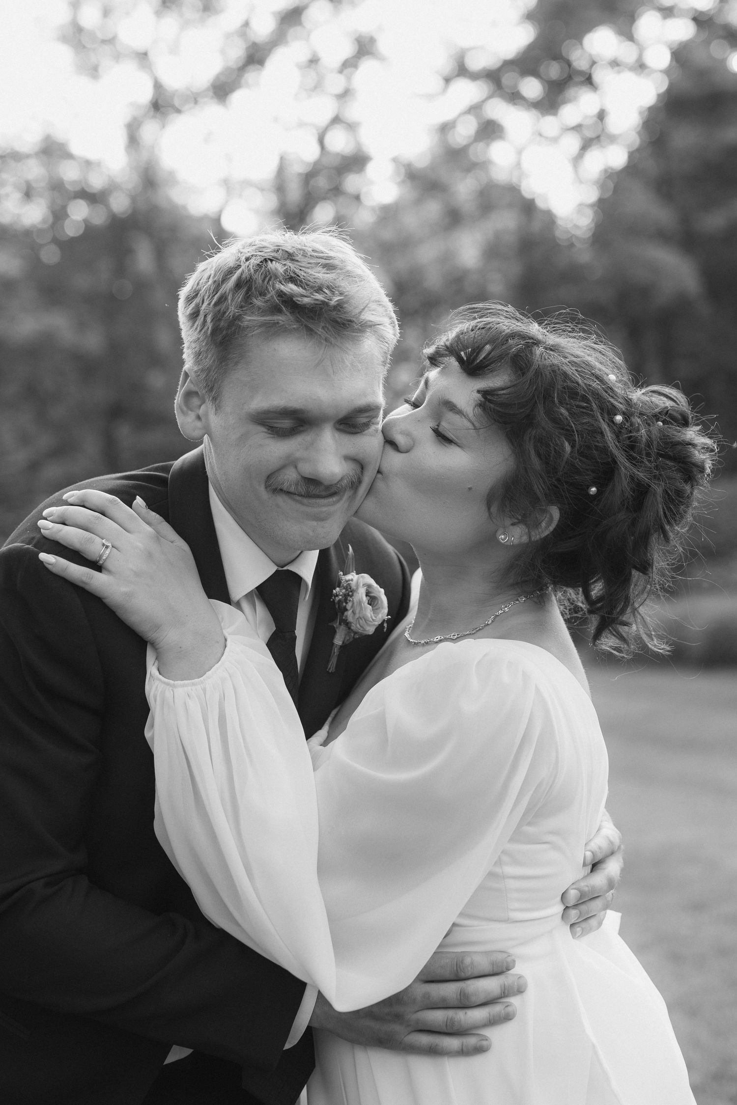 A black and white photograph of a bride and groom embracing and kissing in a scenic outdoor setting.