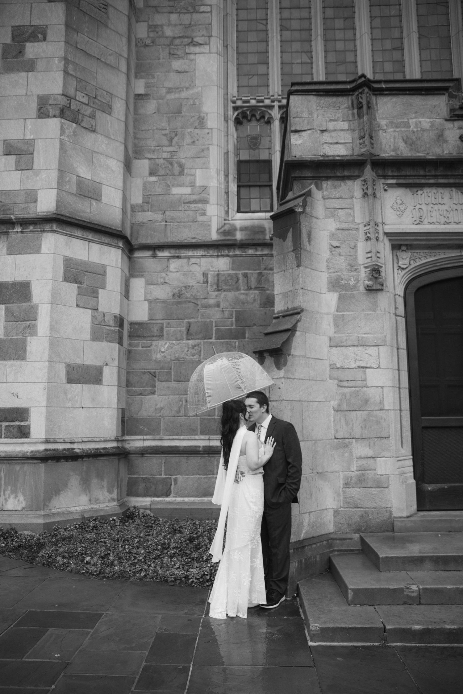 A romantic black and white photo series of a couple sharing intimate moments against a stone church exterior wall.