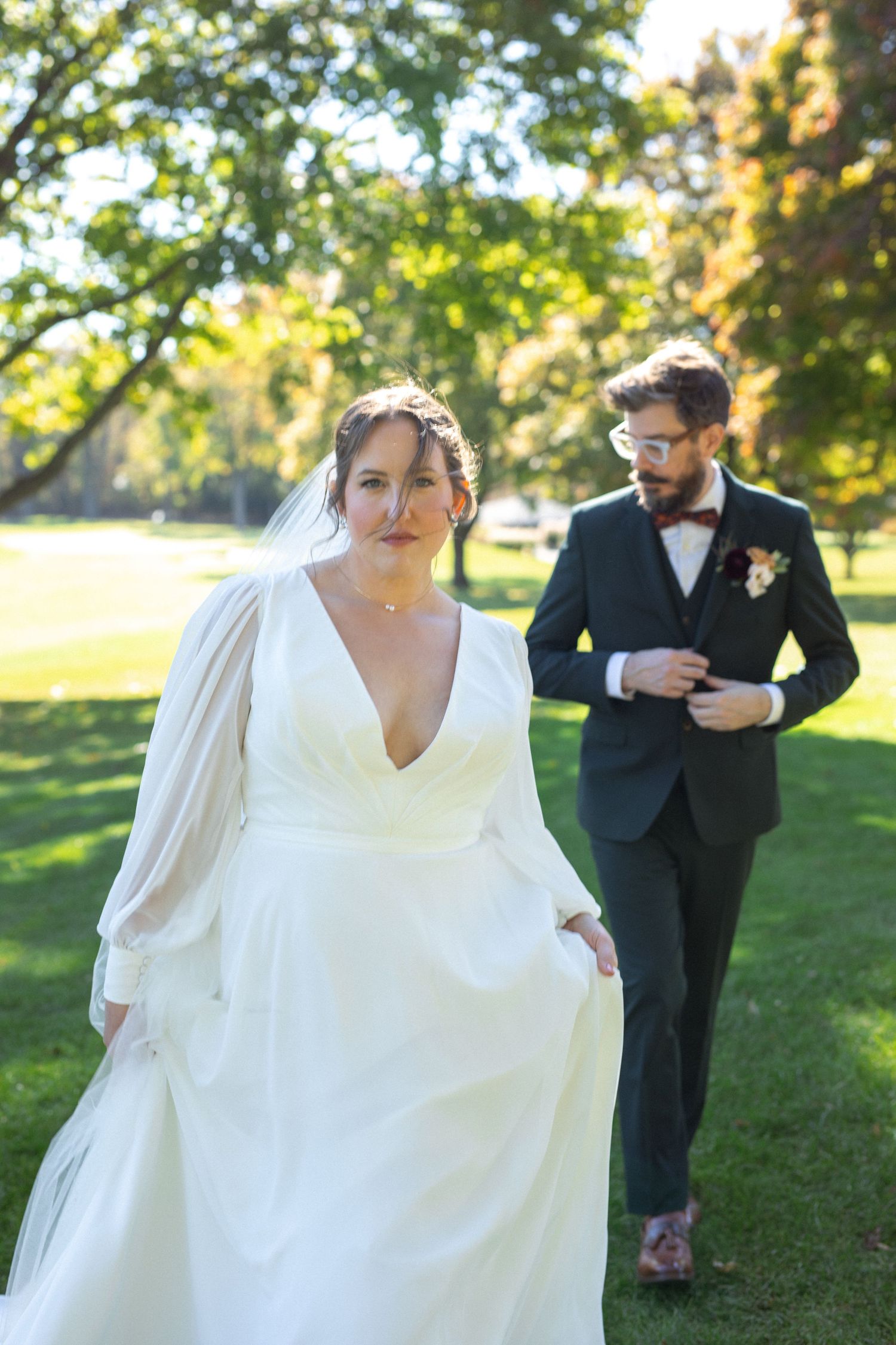 A couple shares a playful moment outdoors as the bride's white dress flows in the sunlight during their wedding photoshoot.