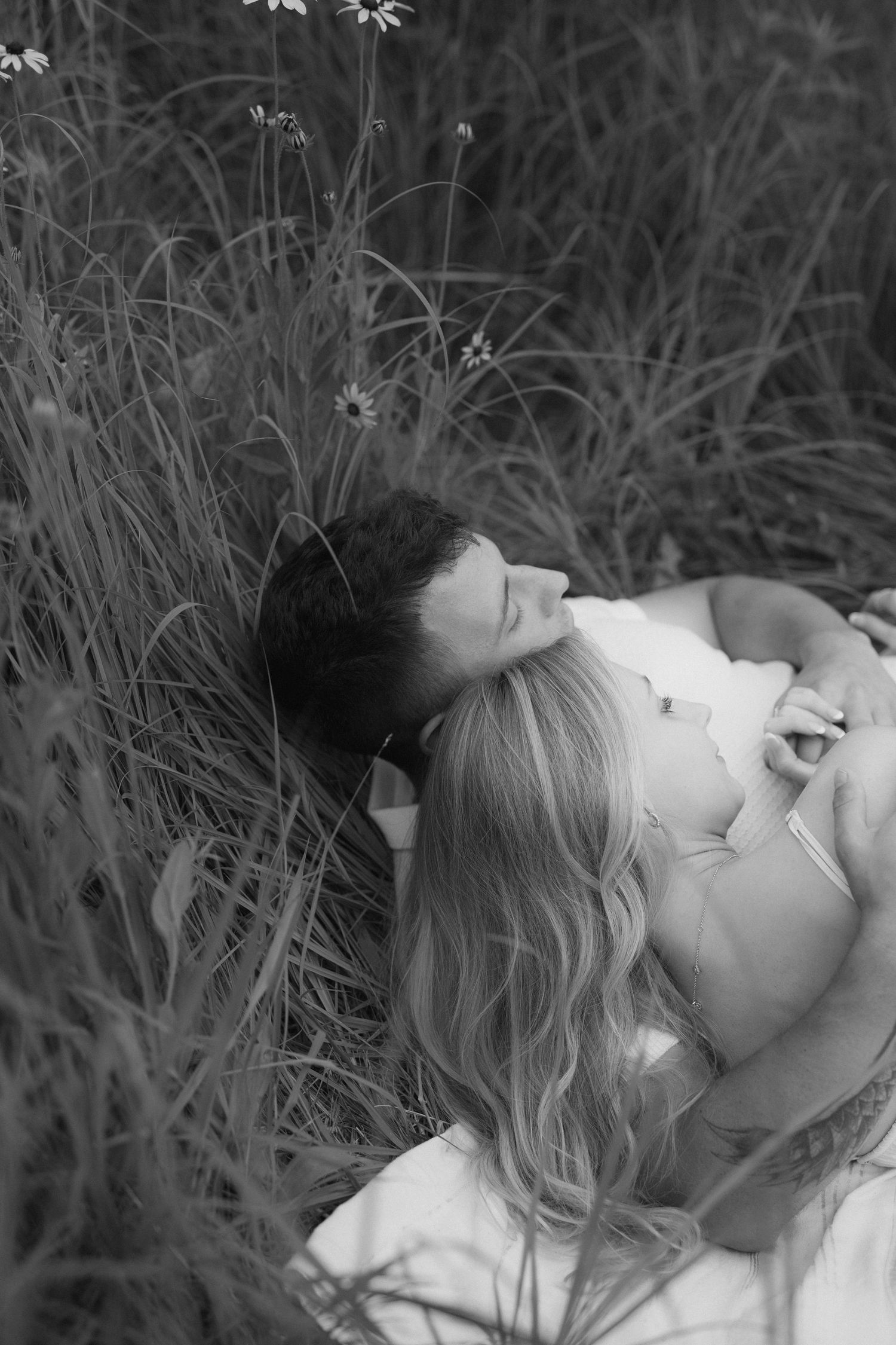 A black and white artistic portrait of someone lying peacefully in tall grass with soft lighting and dreamy atmosphere.