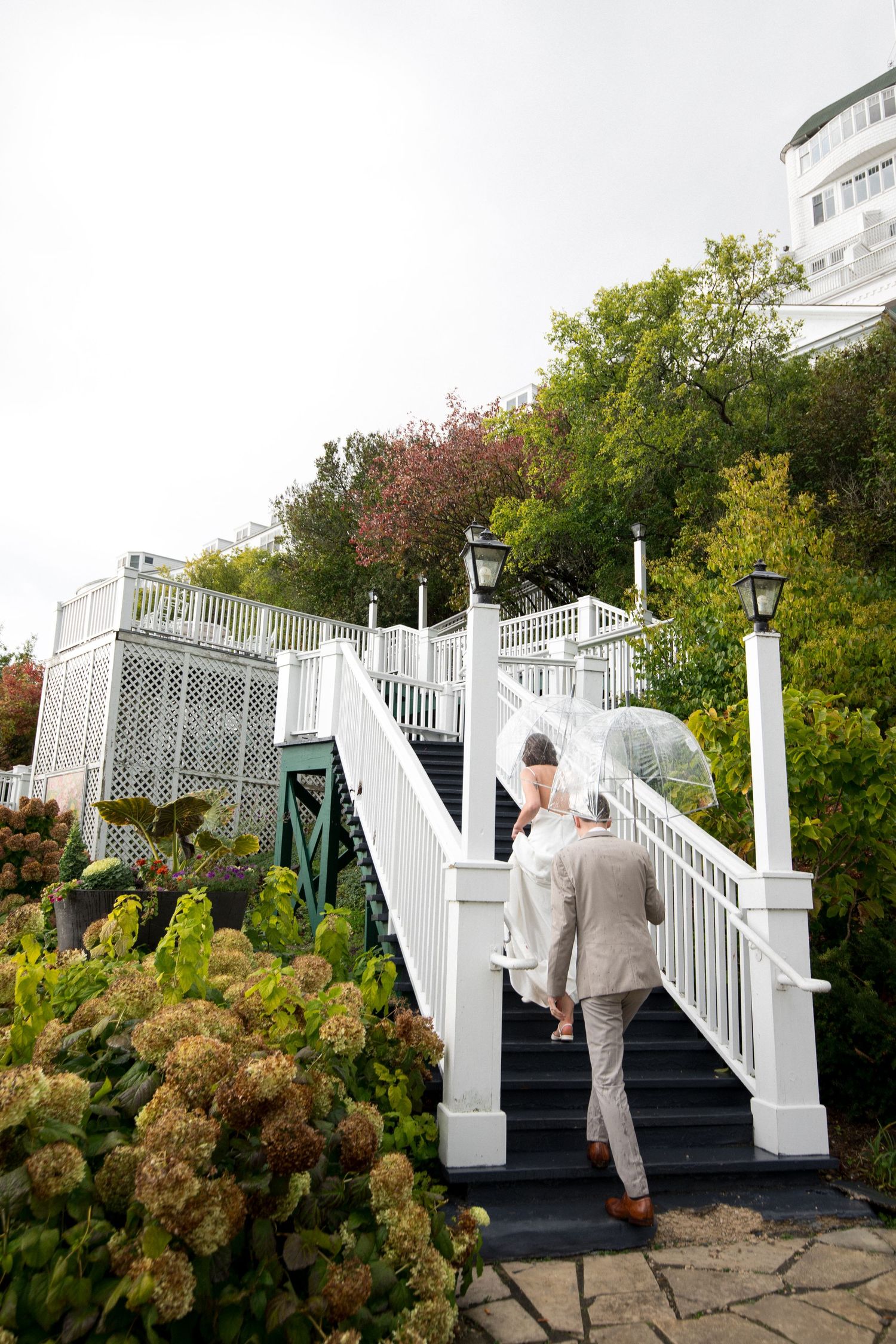 White wooden staircase with ornate railings leads up through lush garden landscaping in an elegant outdoor setting.