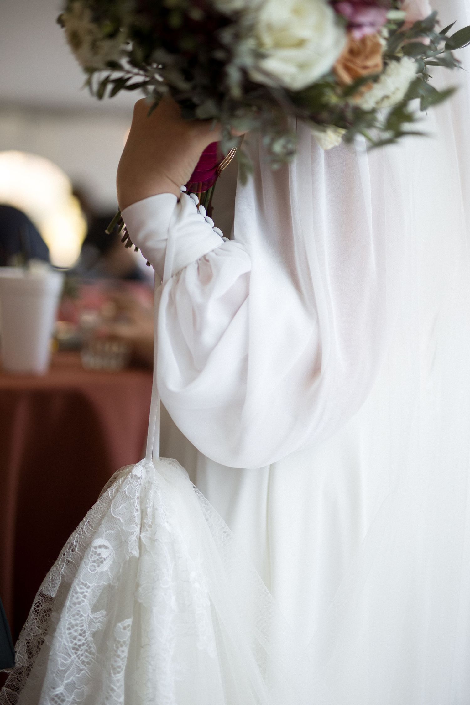 Close-up detail of a white wedding dress with delicate lace and a bouquet with roses and greenery.
