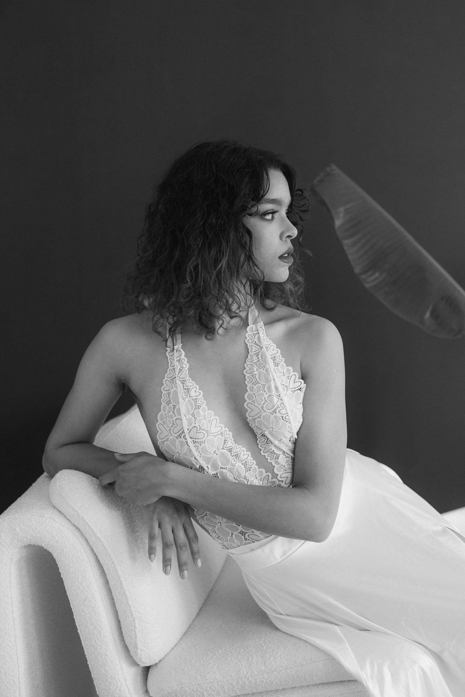 A series of black and white boudoir photos showing a person in white lace loungewear reclining on a light colored surface.