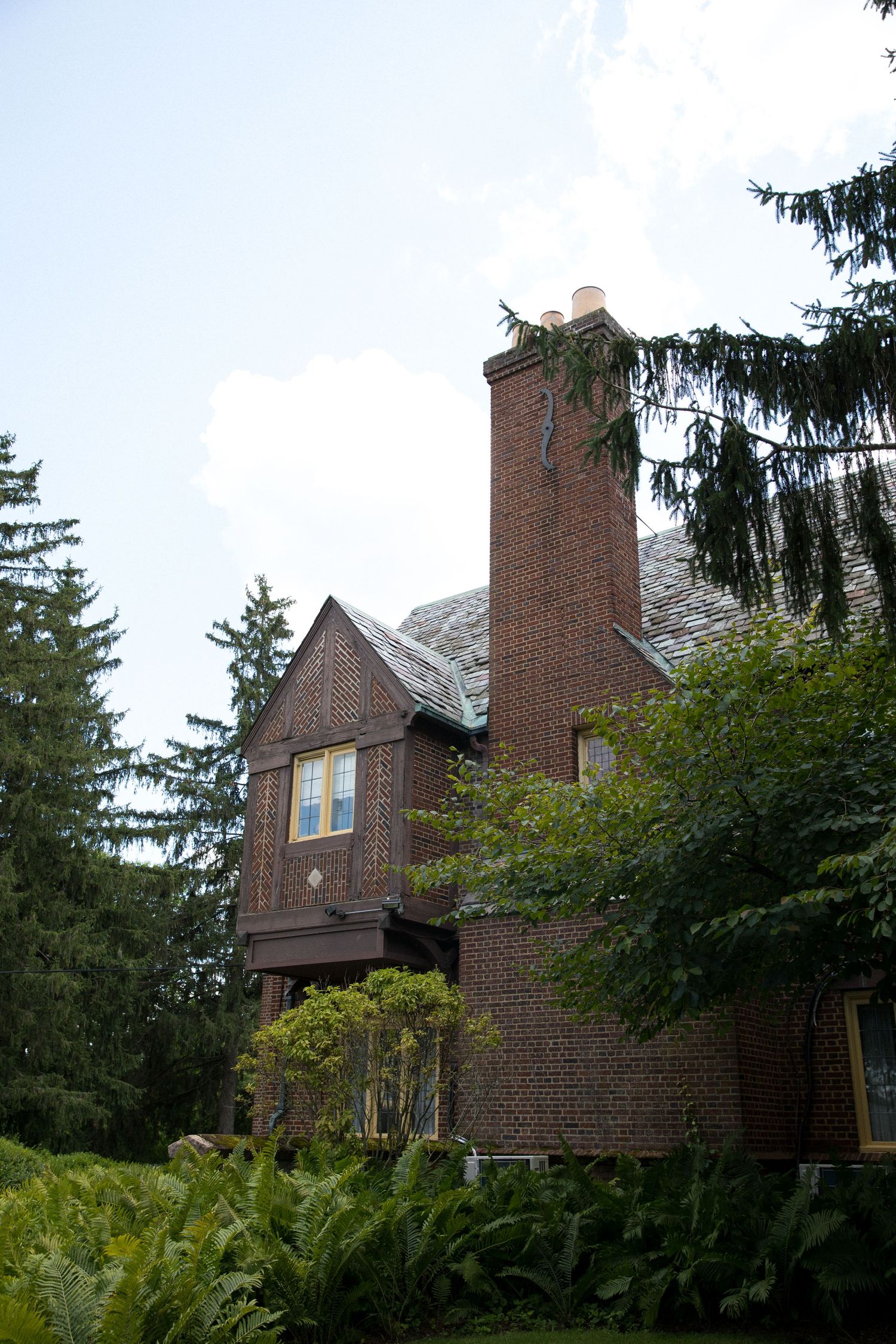 Red brick Tudor-style house with multiple chimneys viewed from different angles among evergreen trees.