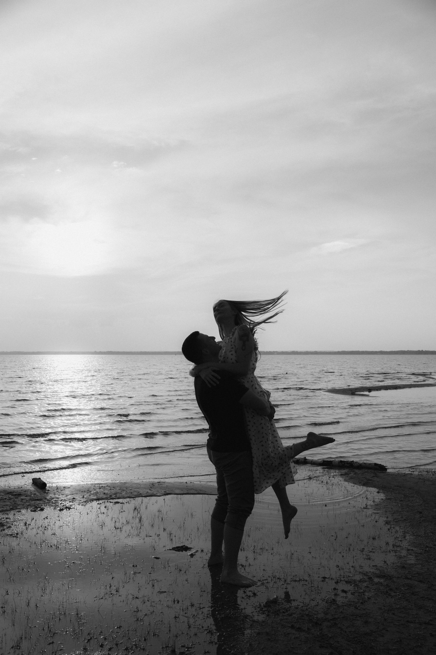 Silhouetted couple embracing on a beach at sunset with flowing hair and waves in the background.