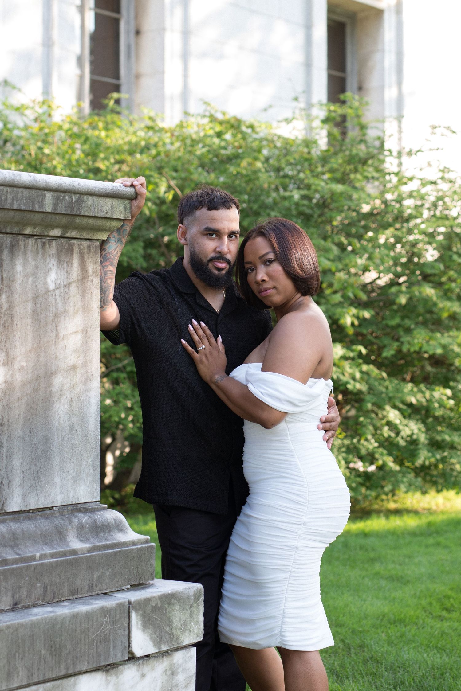 A couple in black and white outfits share tender moments in a garden setting with stone architecture.