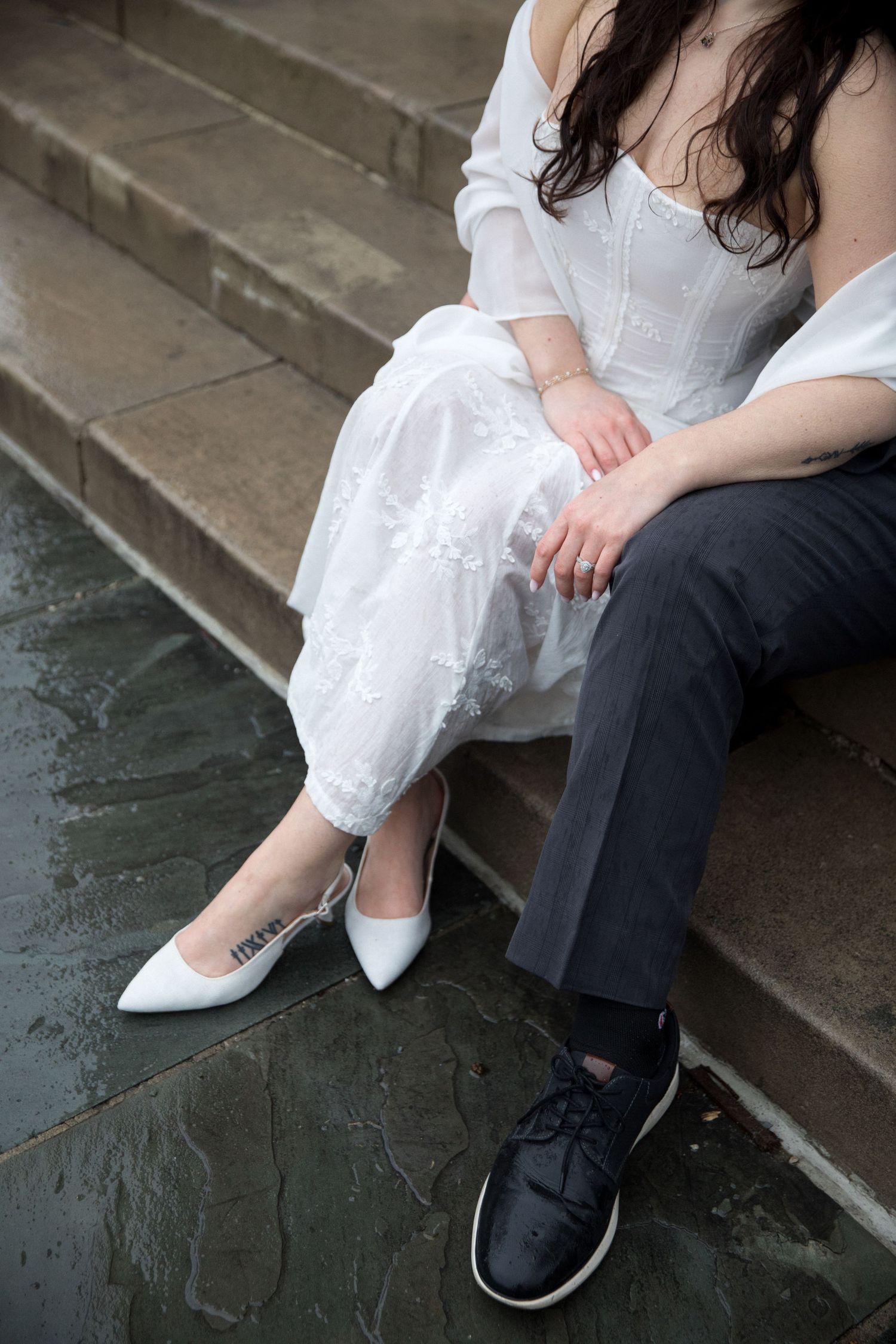 A couple sitting on stone steps wearing contrasting black and white formal attire showing their shoes and lower legs.