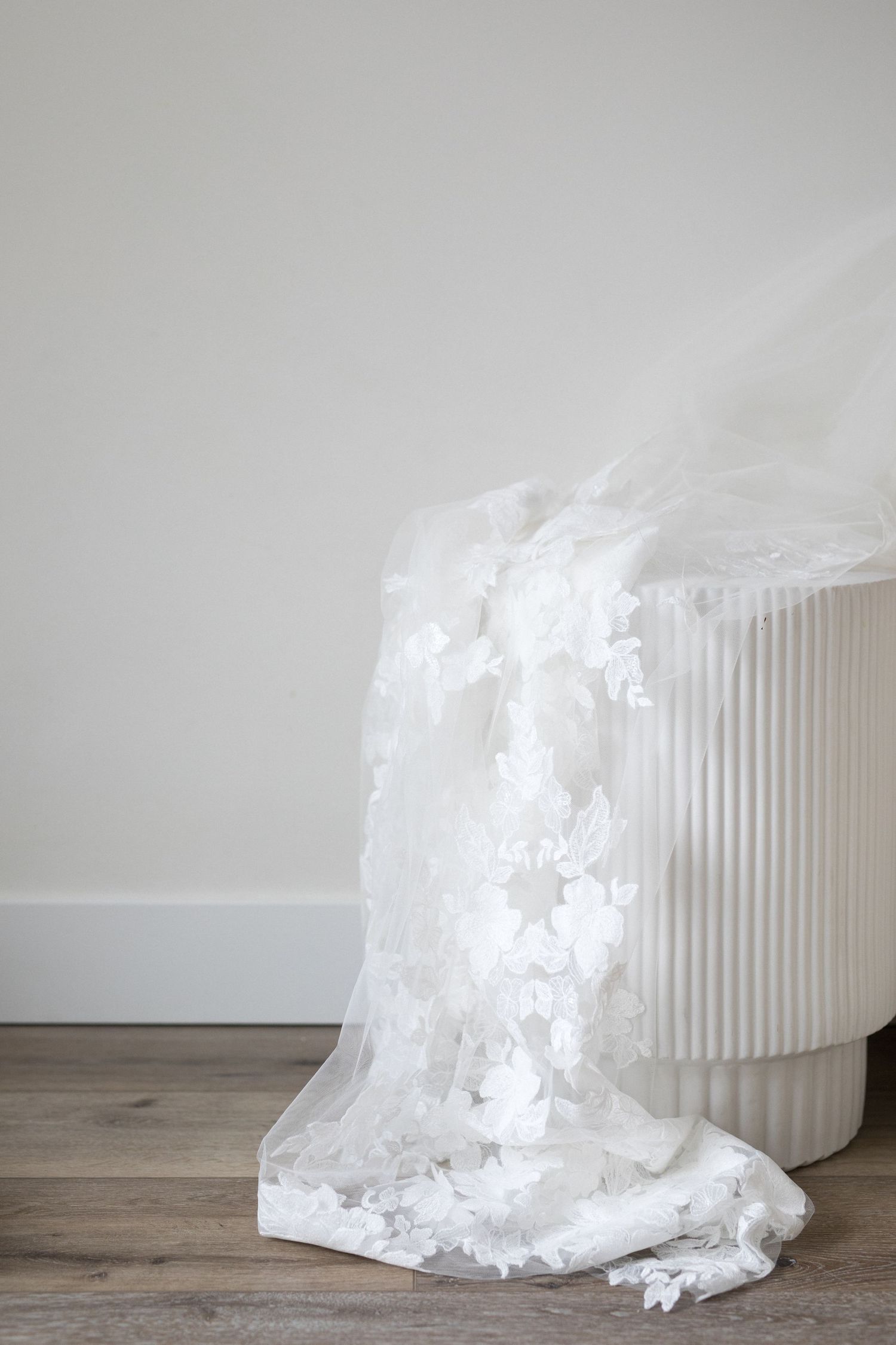 A white cylindrical ceramic vase sits on wooden floor with delicate sheer fabric flowing out like a gentle waterfall.