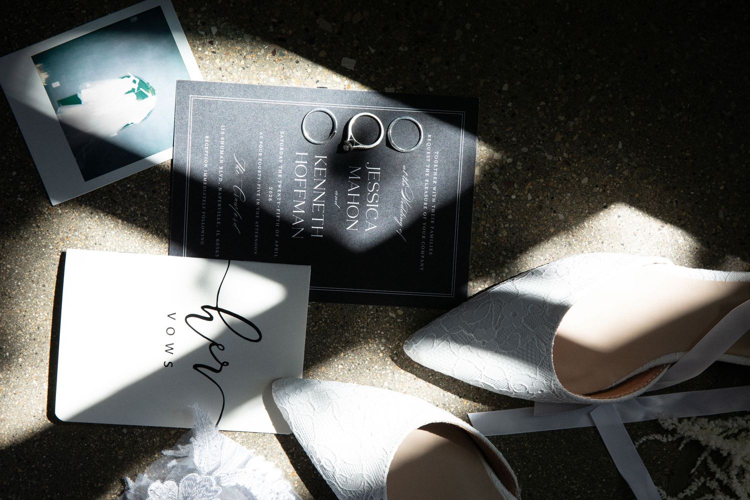 Wedding flat lay with invitation suite, rings, bridal shoes, and polaroid photo in dramatic sunlight.