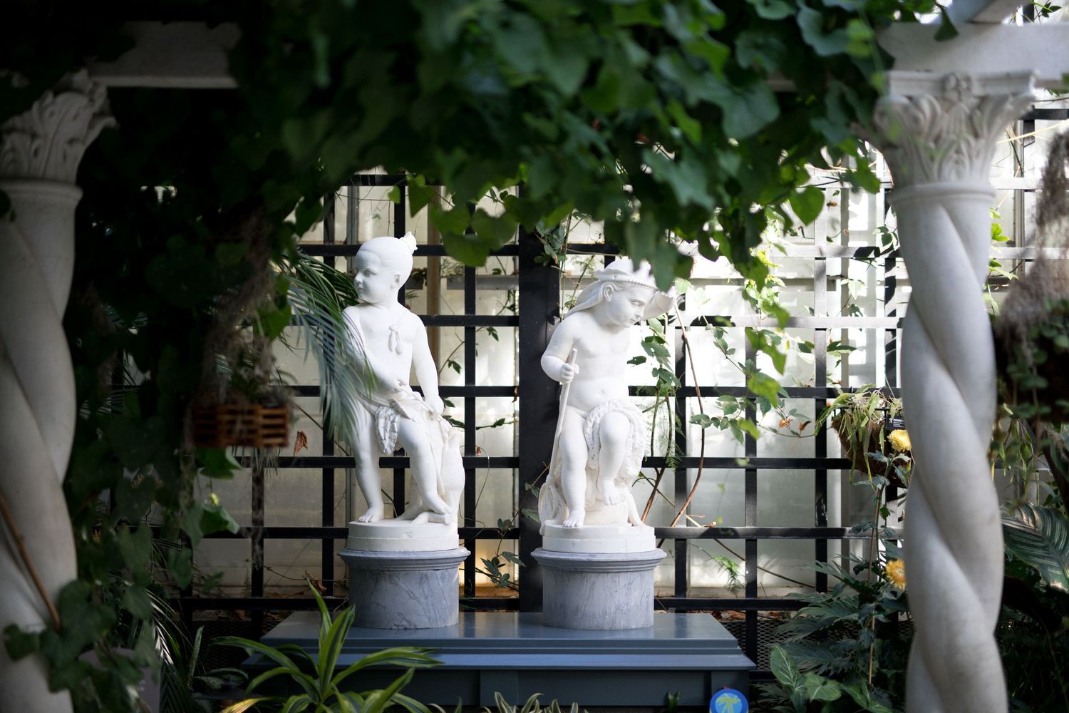 Elegant white statues line a garden path with lush greenery and trees creating a romantic outdoor setting.