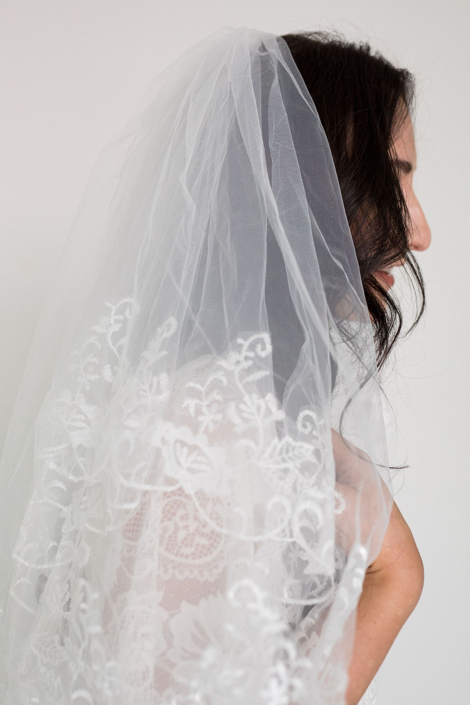 Bride wearing an elegant white lace-trimmed wedding veil, showcasing intricate floral embroidery details.