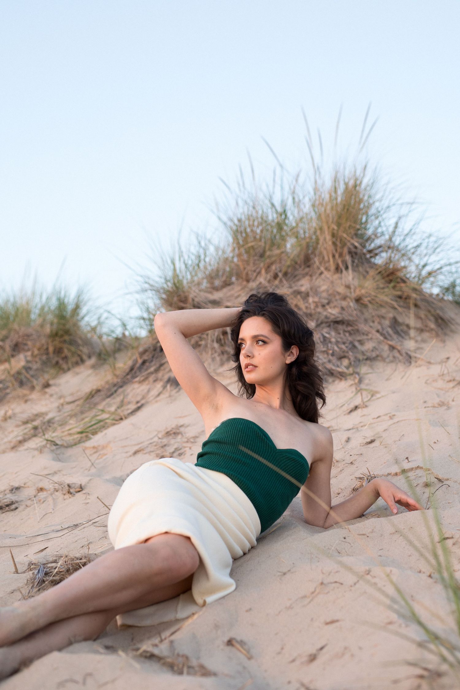 A person in a green top poses gracefully on sandy beach dunes at sunset.