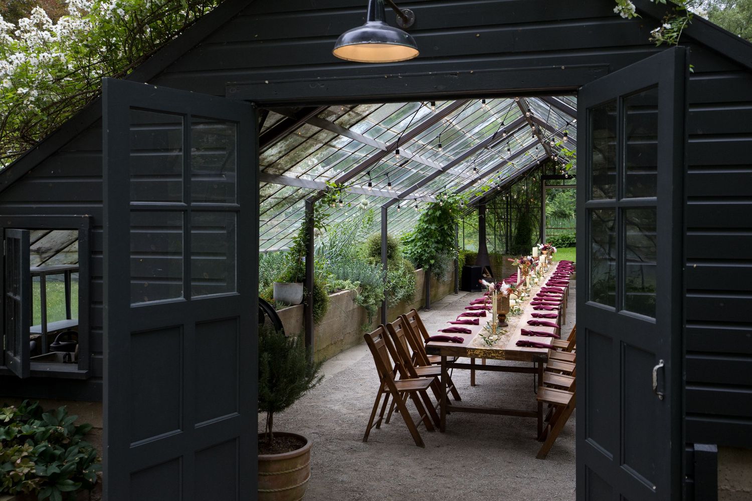 A rustic greenhouse with dark wood exterior features multiple seating areas and glass panels for natural light.