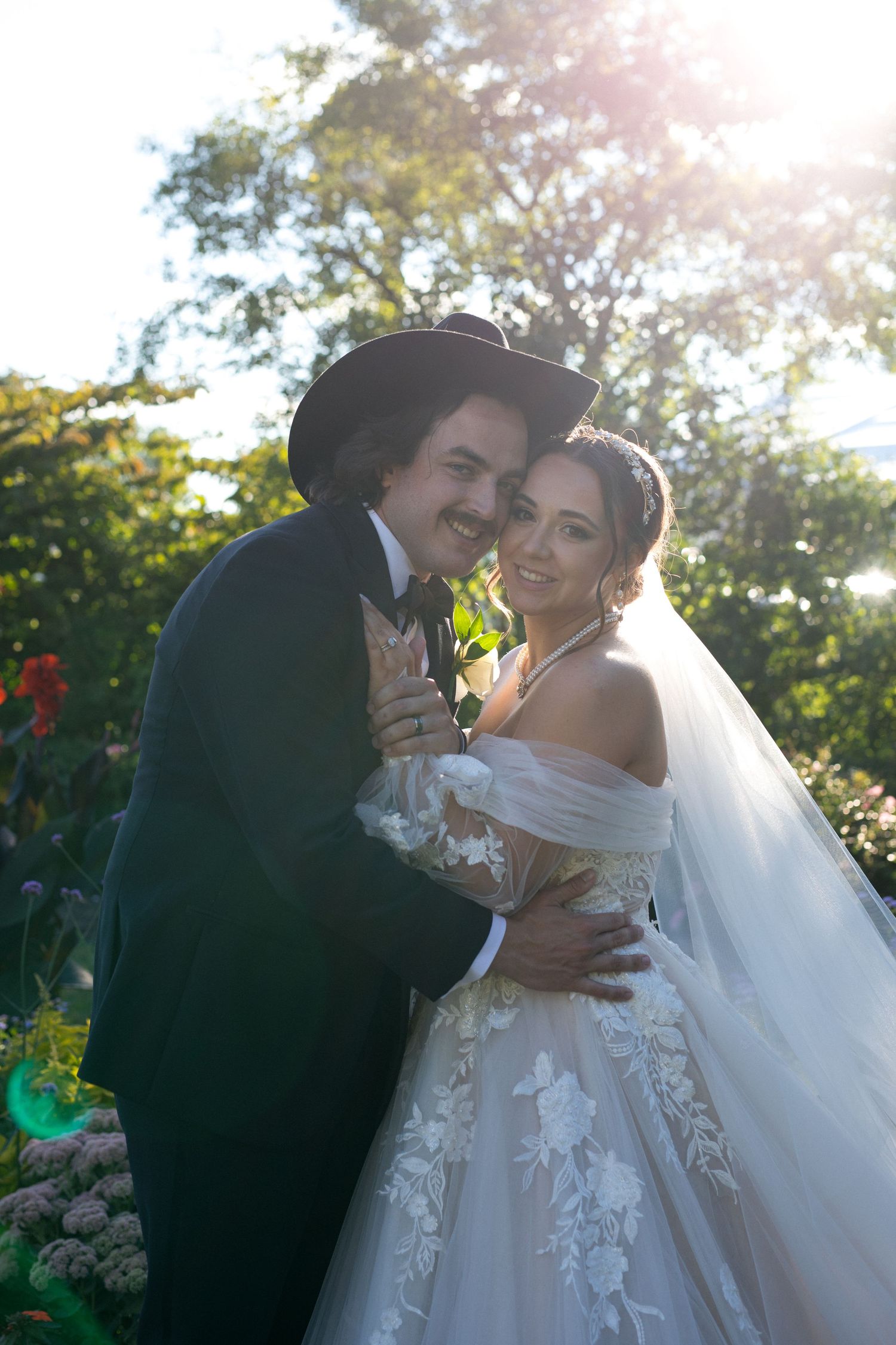 Romantic outdoor wedding moment captured in golden sunlight among blooming garden flowers.