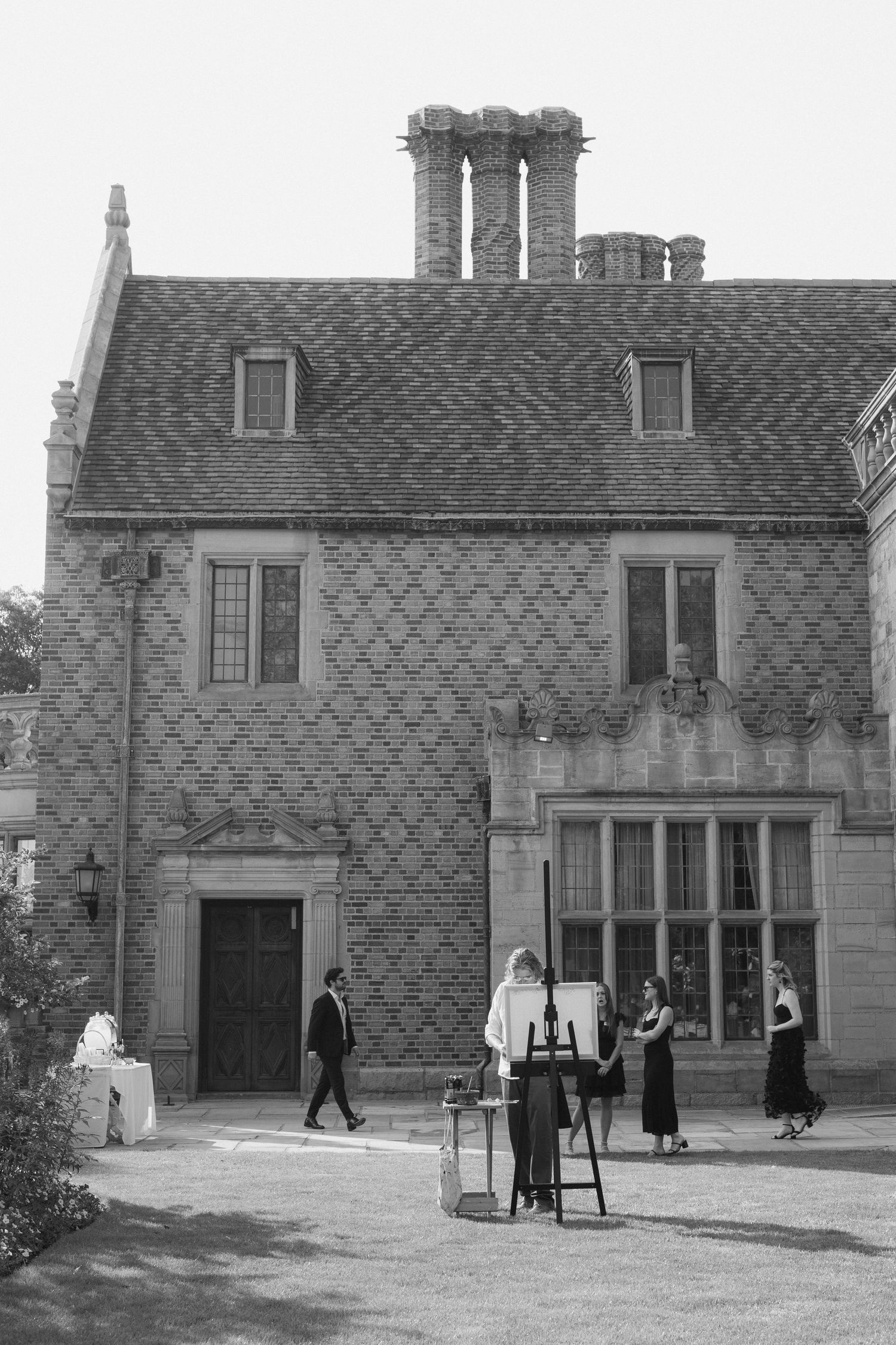 Black and white photo of wedding attendees outside a stone building with diamond-patterned walls.