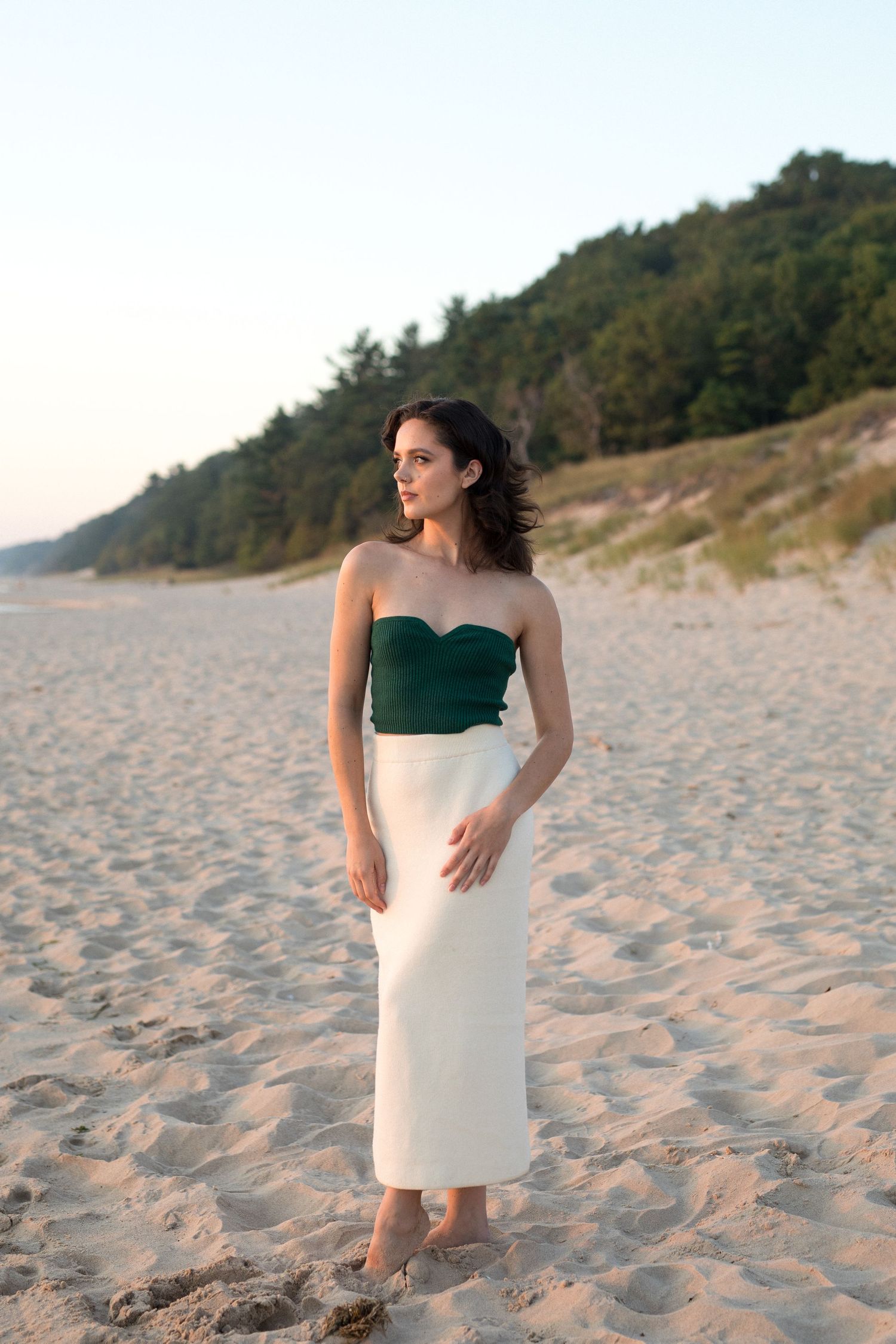 Elegant strapless dress with emerald green top and white skirt photographed on sandy beach at sunset.