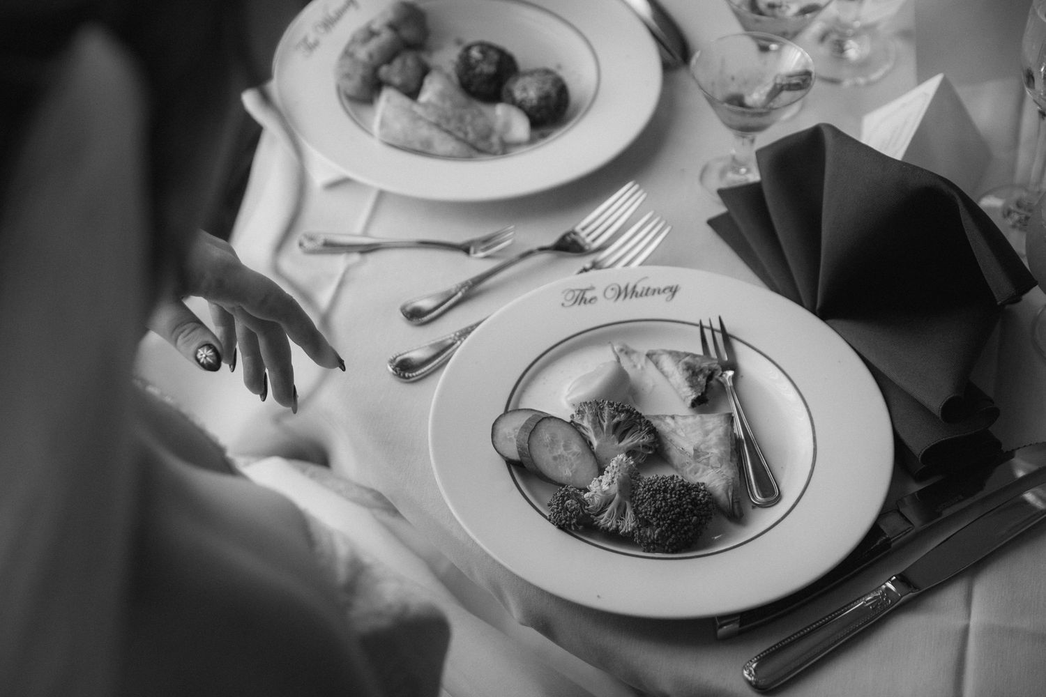Black and white overhead view of elegant table setting with plated meals and formal dining utensils.