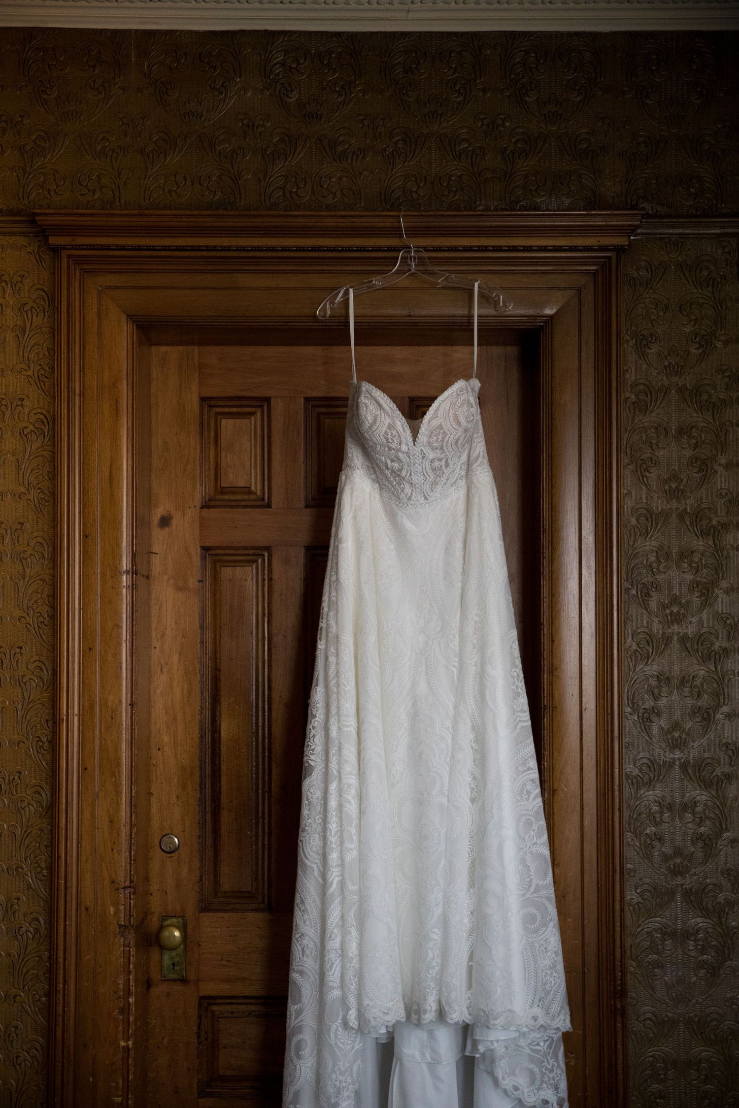 Five elegant white lace wedding dresses hanging on wooden doors against a dark textured wall.