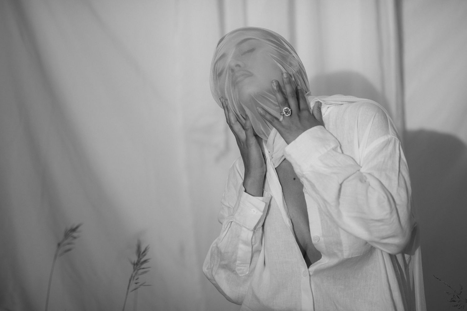 A person in a white shirt covers their face with both hands in a dramatic black and white photograph.