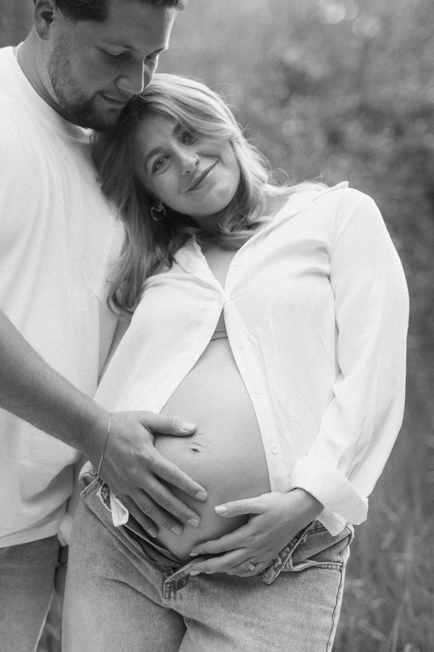Black and white photo of a couple tenderly cradling a pregnant belly outdoors, capturing a joyful maternity moment.