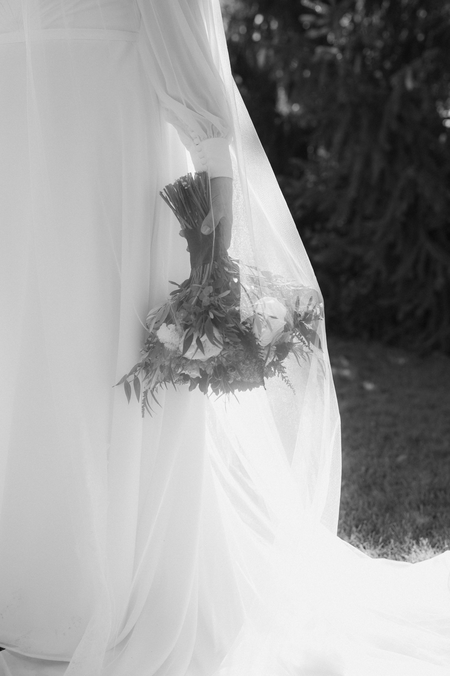 Black and white photo of a wedding dress with a bouquet silhouetted through flowing white fabric.