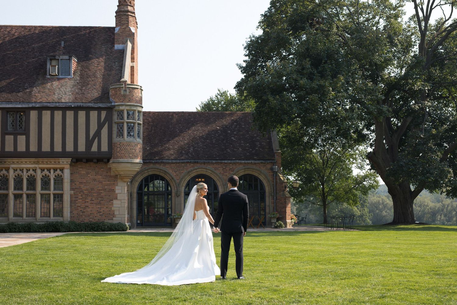 Elegant outdoor wedding ceremony at a historic Tudor-style brick manor with manicured lawn.
