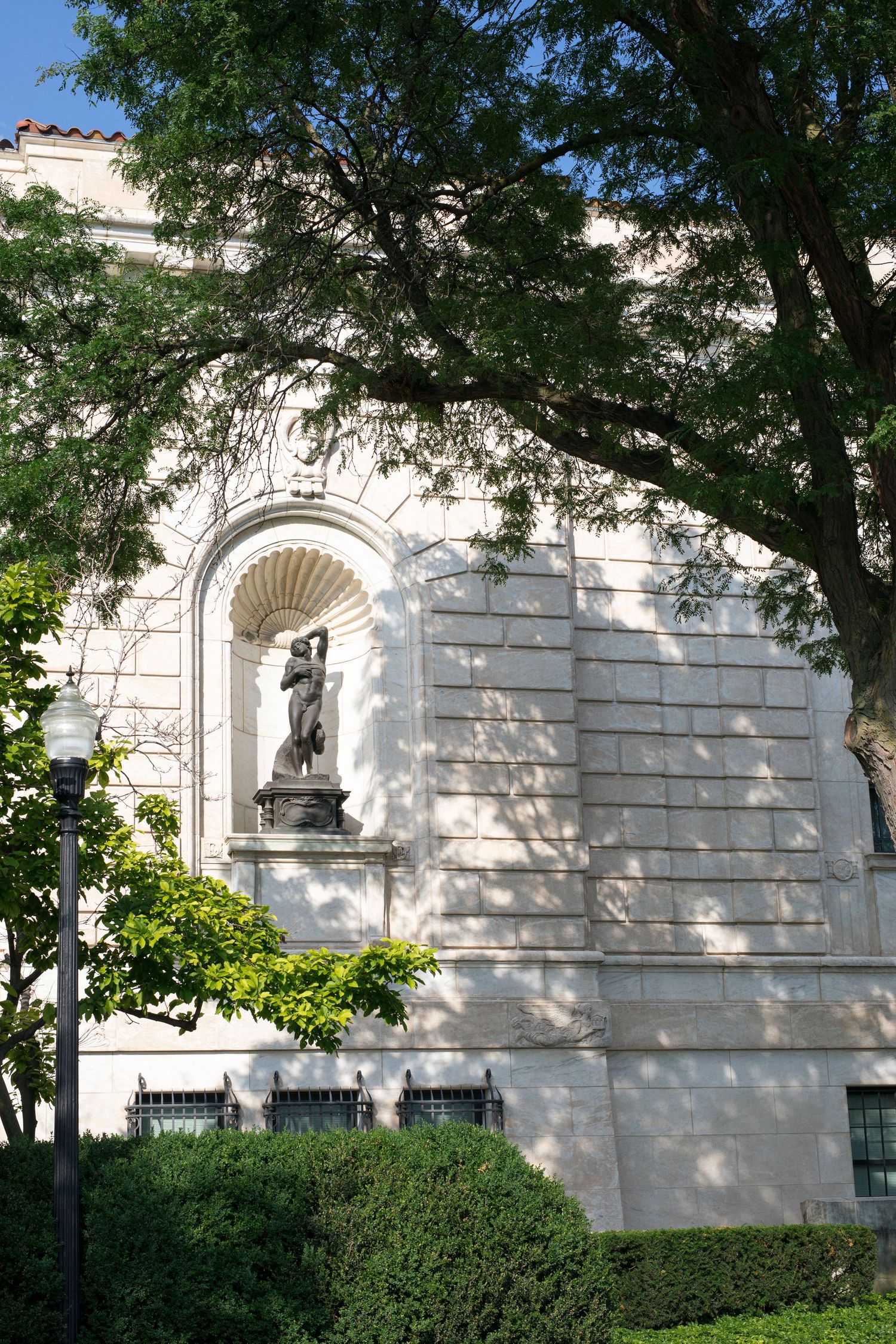 A panoramic view of white stone building walls with arched details and green trees casting shadows on the architecture.