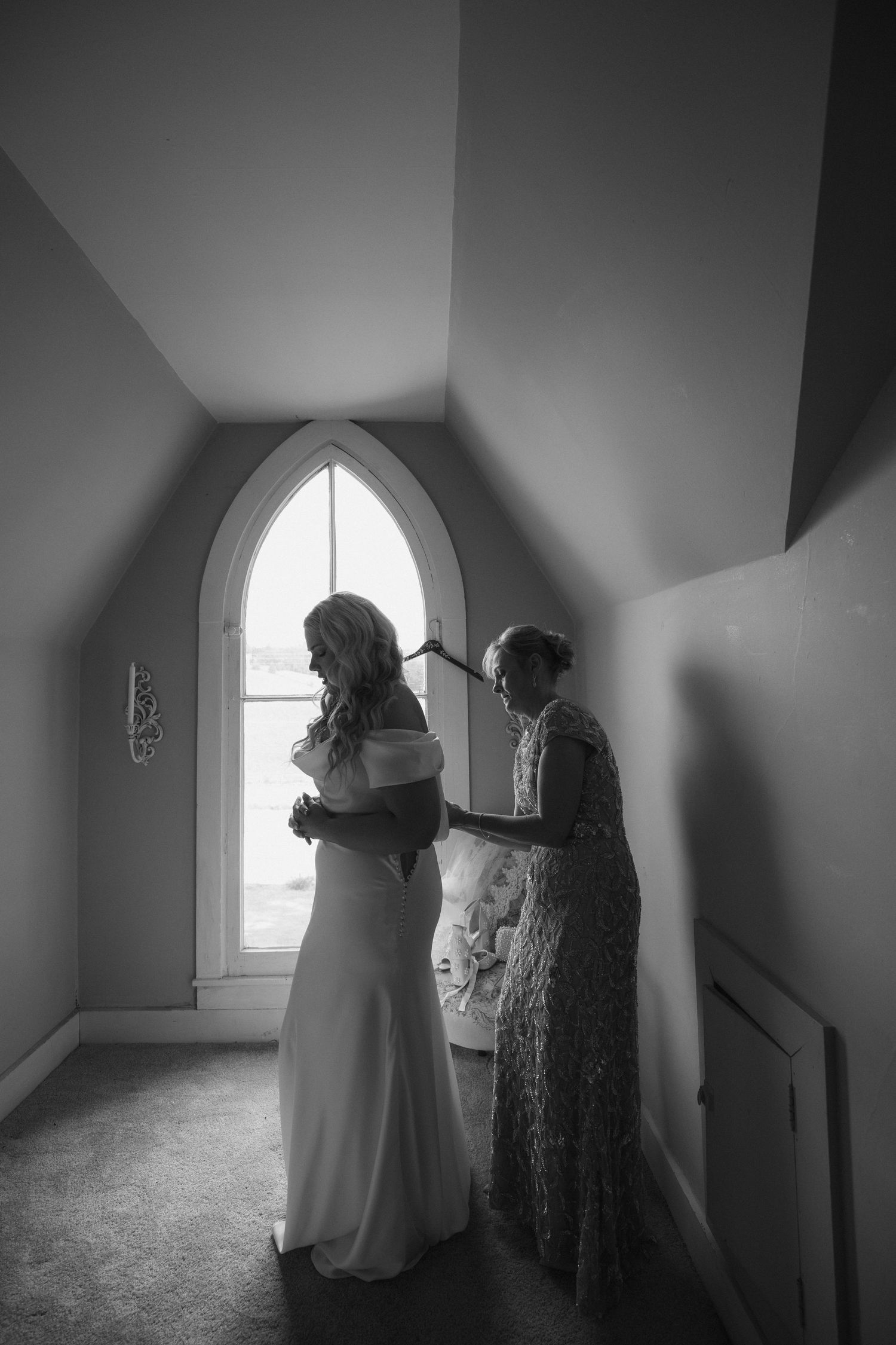 Two figures stand silhouetted in a stark hallway with an arched window casting dramatic light and shadow.