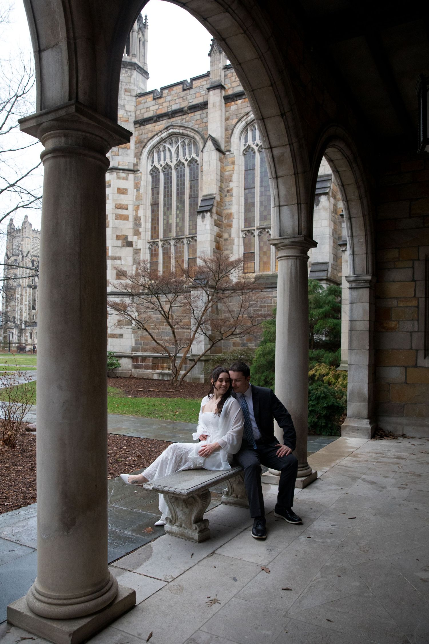 A couple sits together under stone archways in a Gothic-style courtyard walkway.