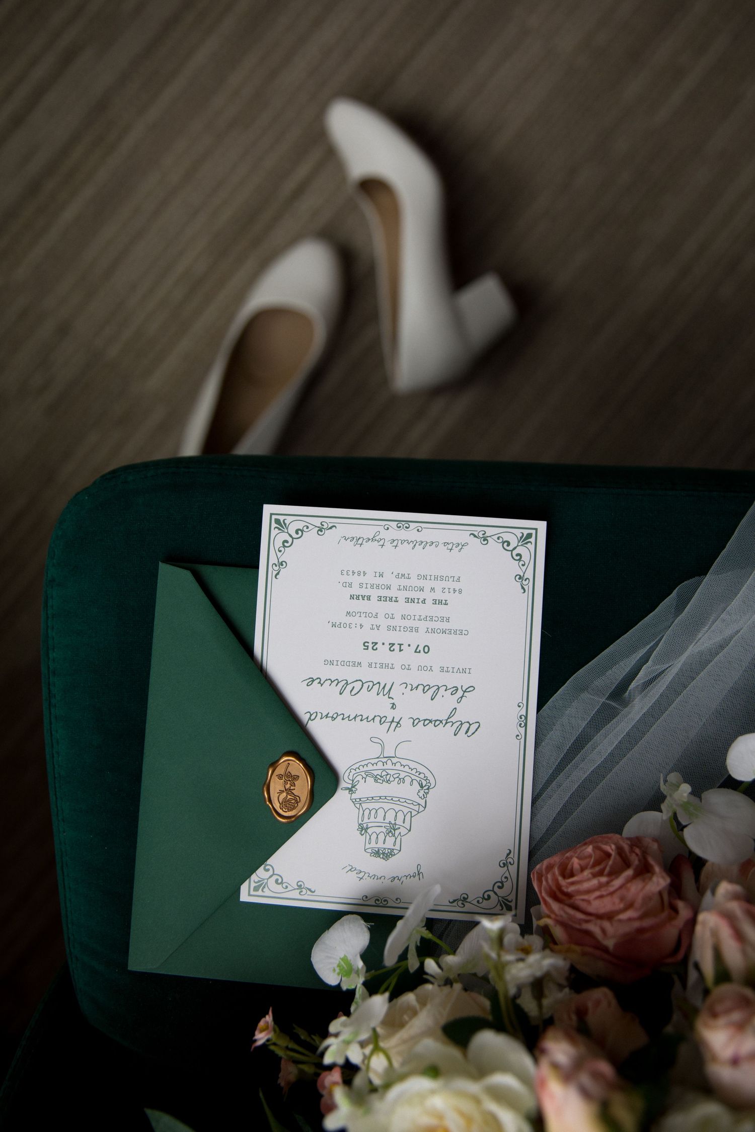 Wedding invitations and delicate flowers arranged on a dark green velvet surface create an elegant flat lay composition.