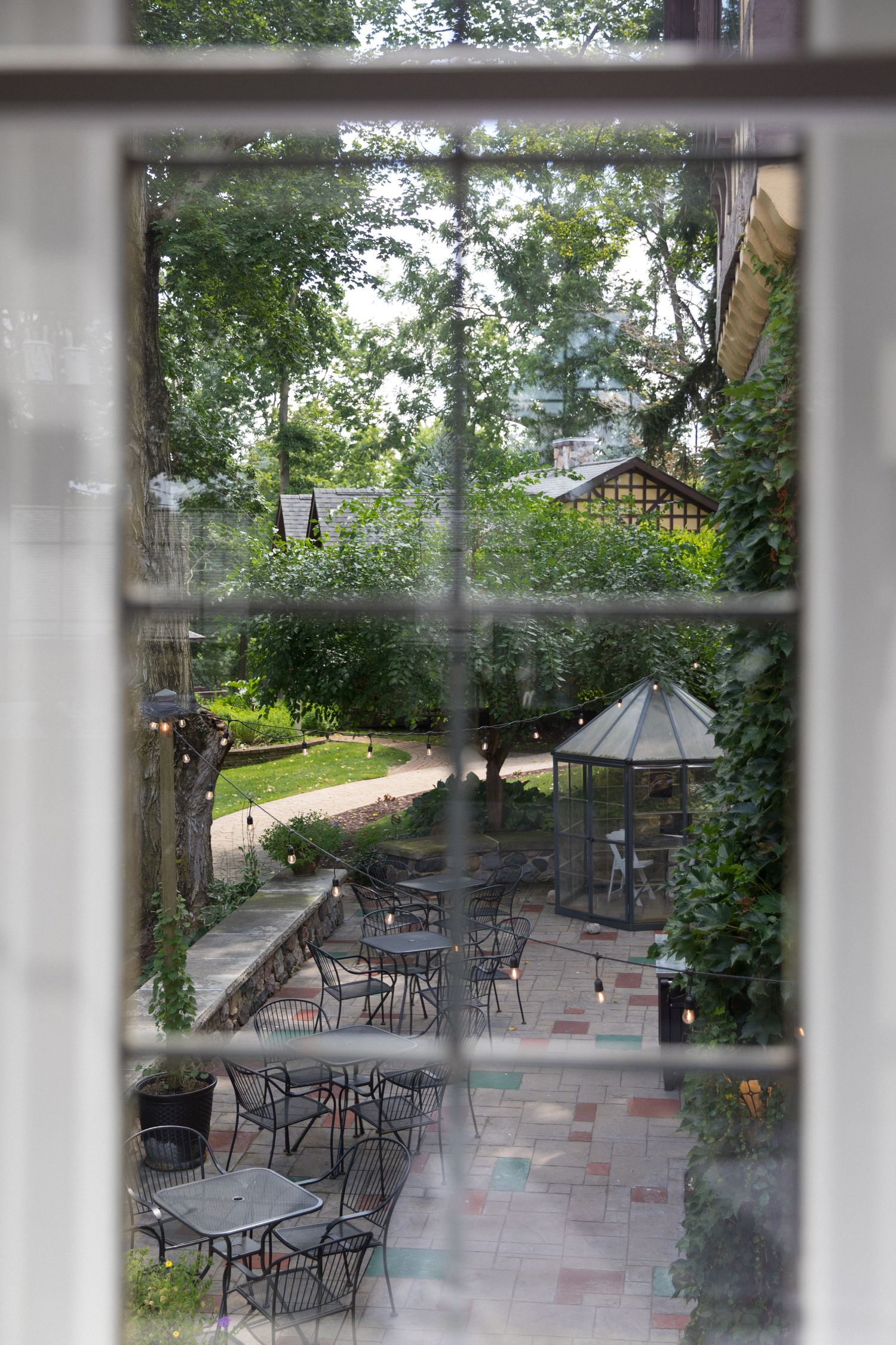 Outdoor restaurant patio with wrought iron furniture and pink tiled flooring viewed through window panes.