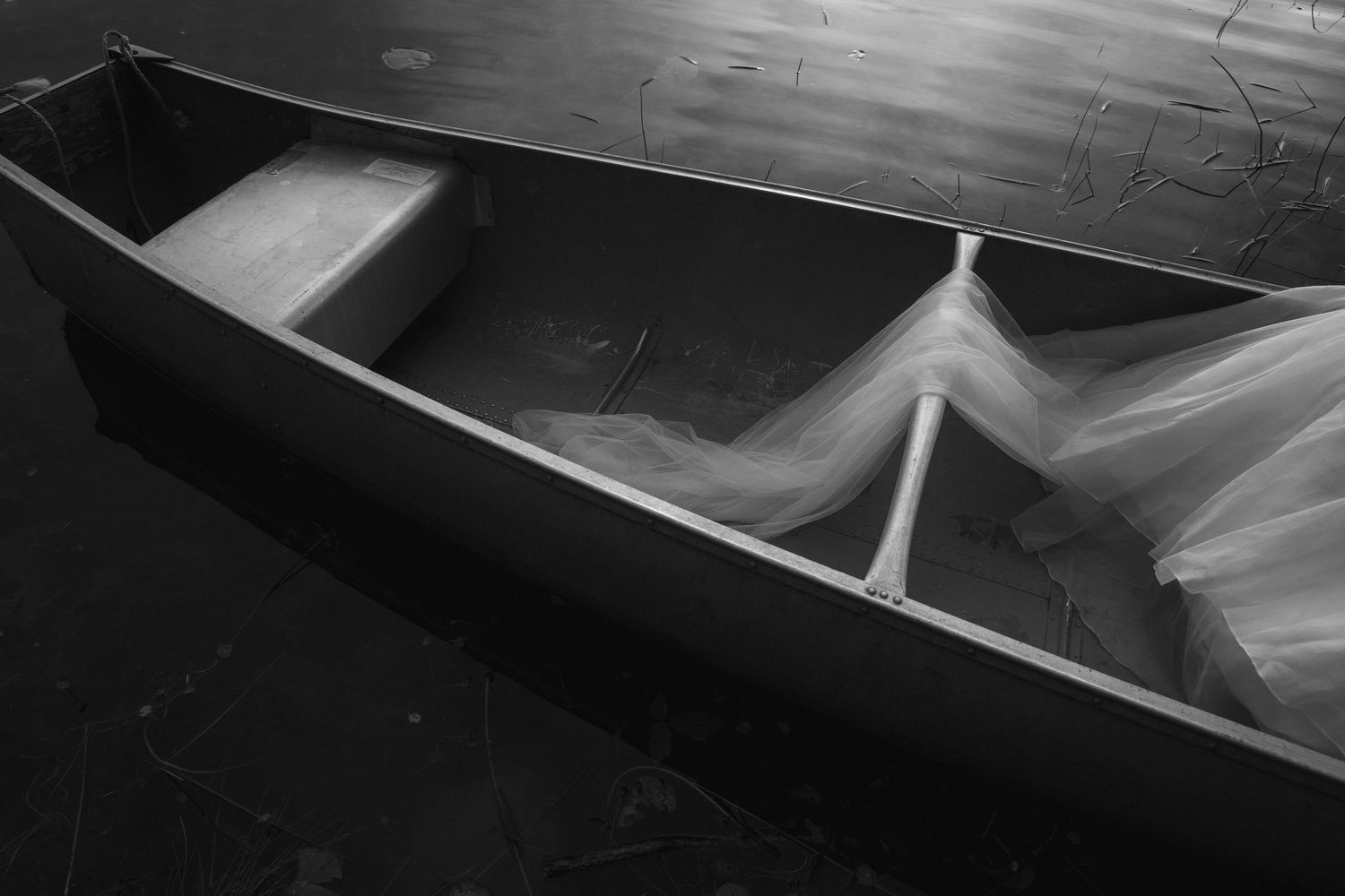 Black and white aerial view of a weathered wooden canoe with fishing net inside, captured in moody low-light photography.