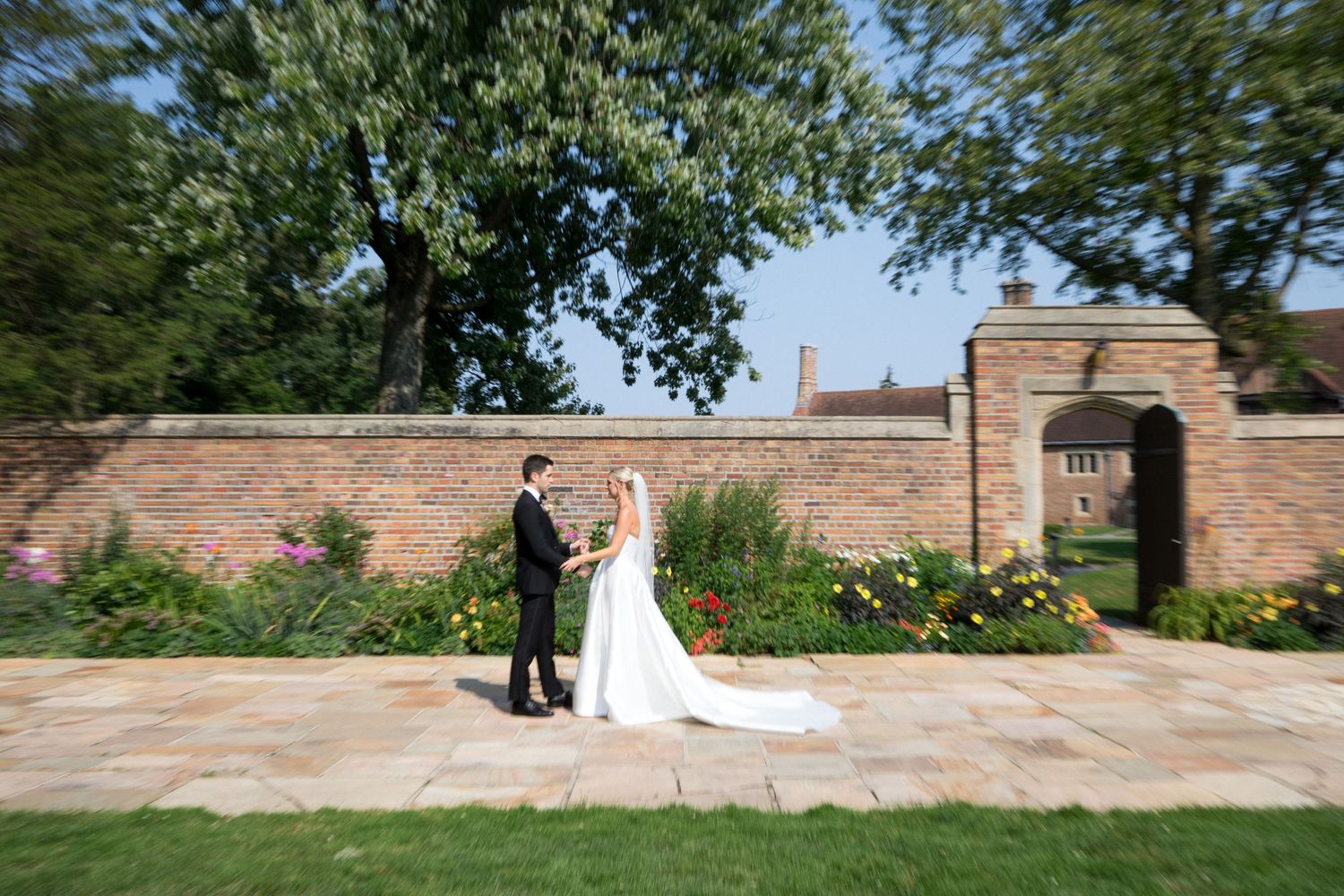 A couple shares a romantic moment in front of a stone garden wall with lush greenery on a sunny day.