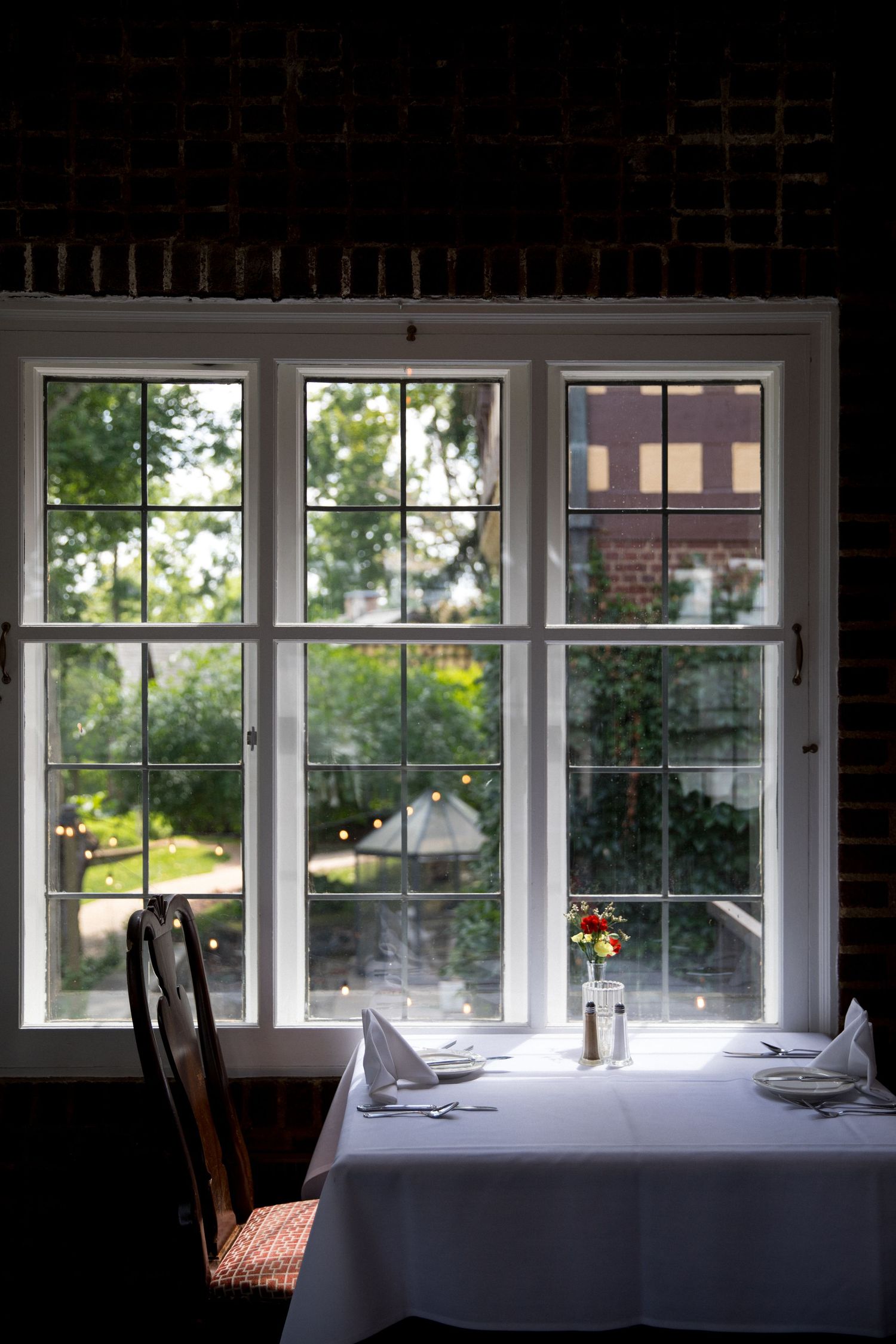 A series of bright windows with white frames in a restaurant dining room setting with white tablecloths.