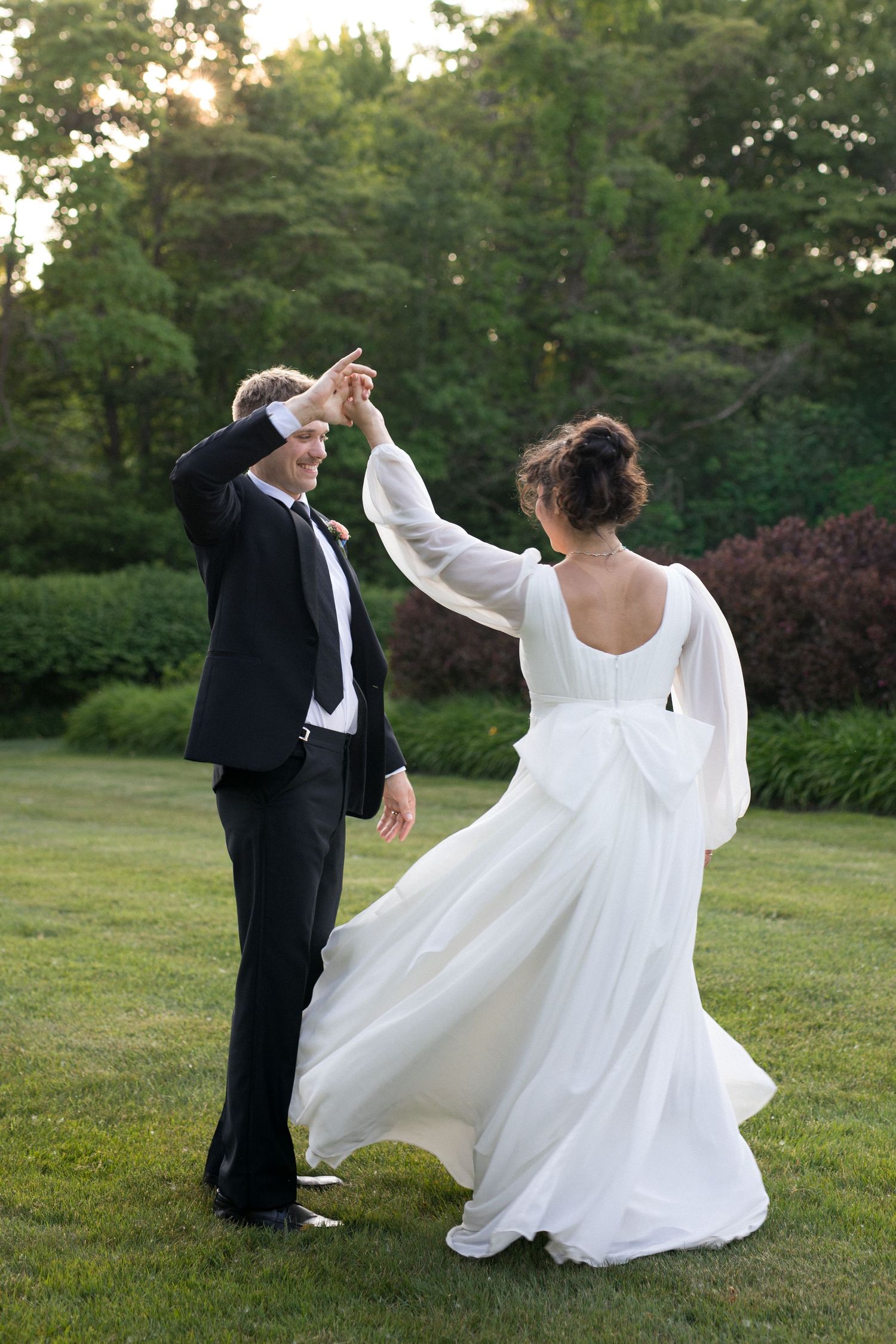 A bride and groom dance together in a garden setting on their wedding day.
