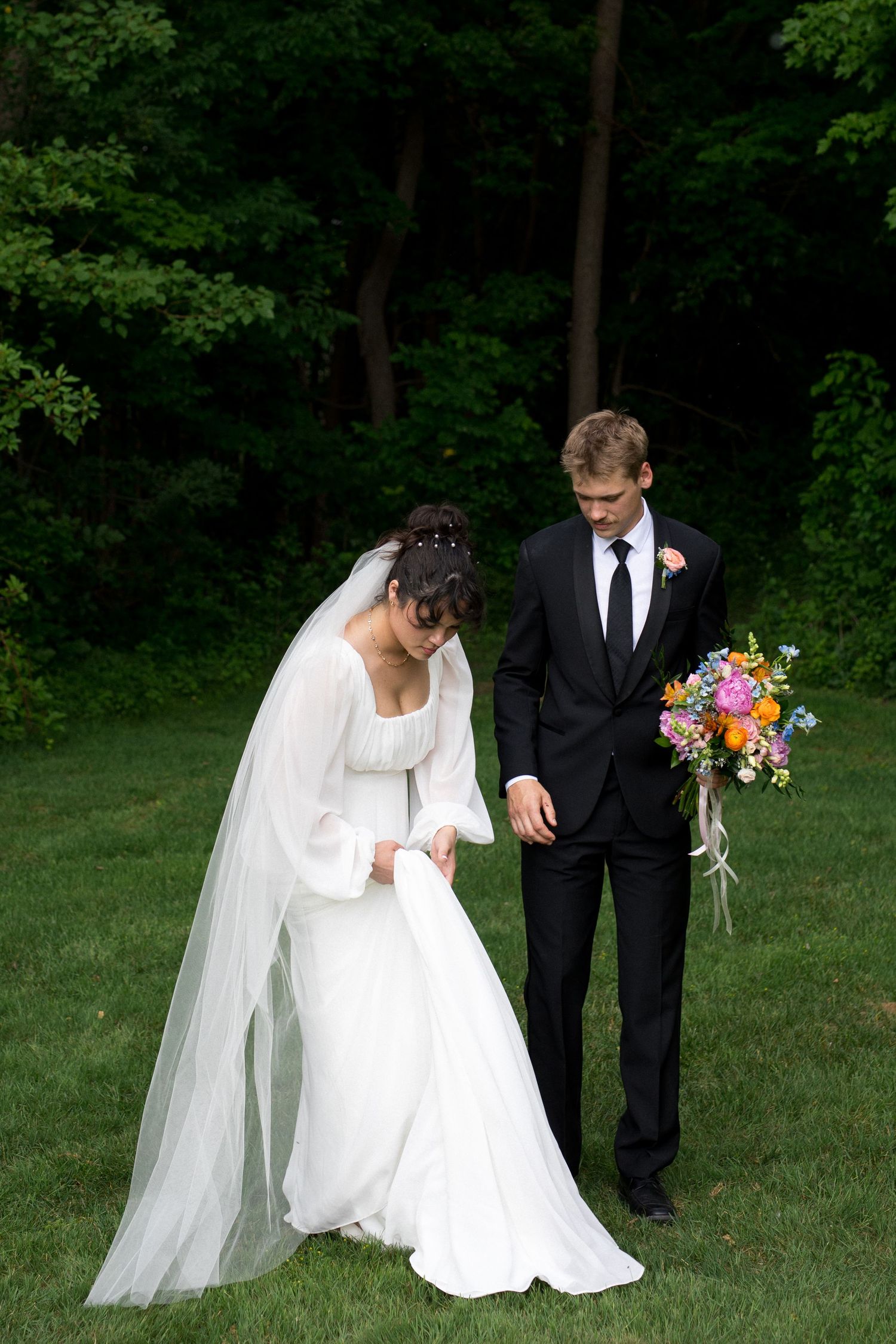A couple in wedding attire share a tender moment outdoors in a lush green garden setting.